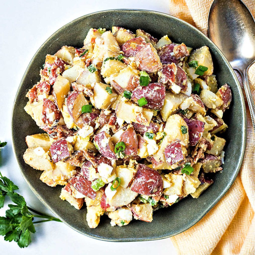 red potato salad on a green plate with a yellow napkin and serving spoon, Italian parsley to the side.