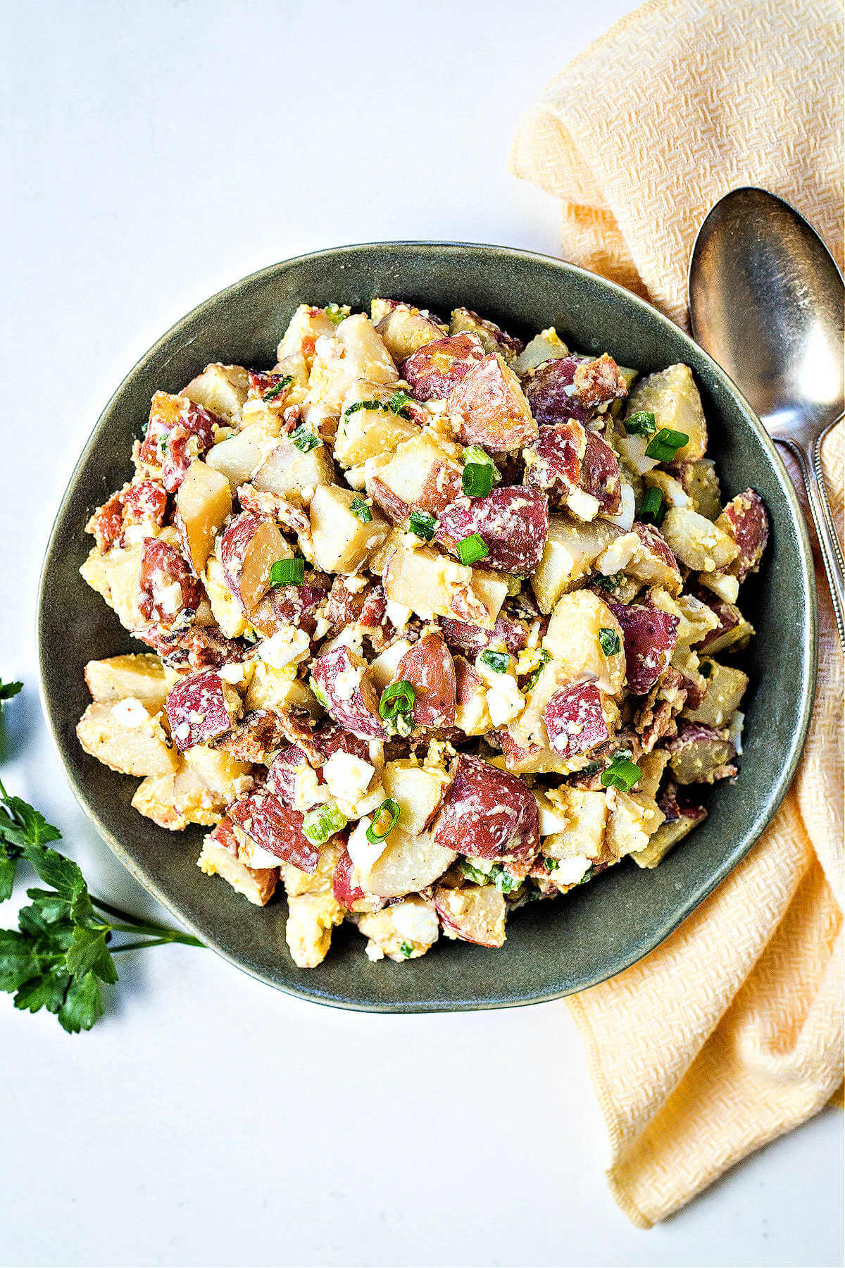 red potato salad on a green plate with a yellow napkin and serving spoon, Italian parsley to the side.