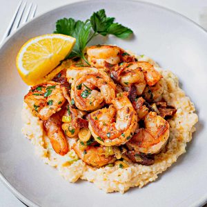 shrimp ladled on top of a bed of stone ground cheese grits with a lemon wedge and parsley.