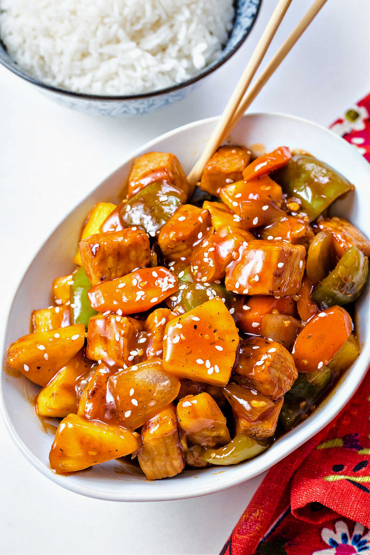 sweet and sour pork in a white bowl with chopsticks with a bowl of rice in the background.