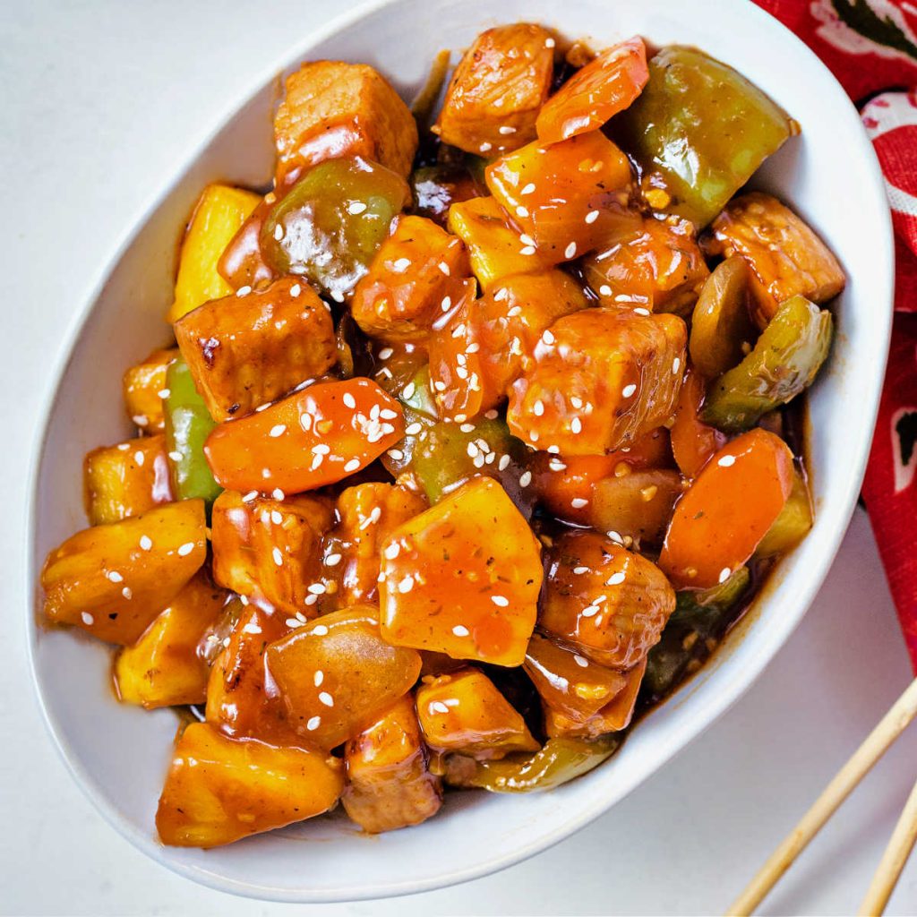sweet and sour pork garnished with sesame seeds in a white bowl on a table.