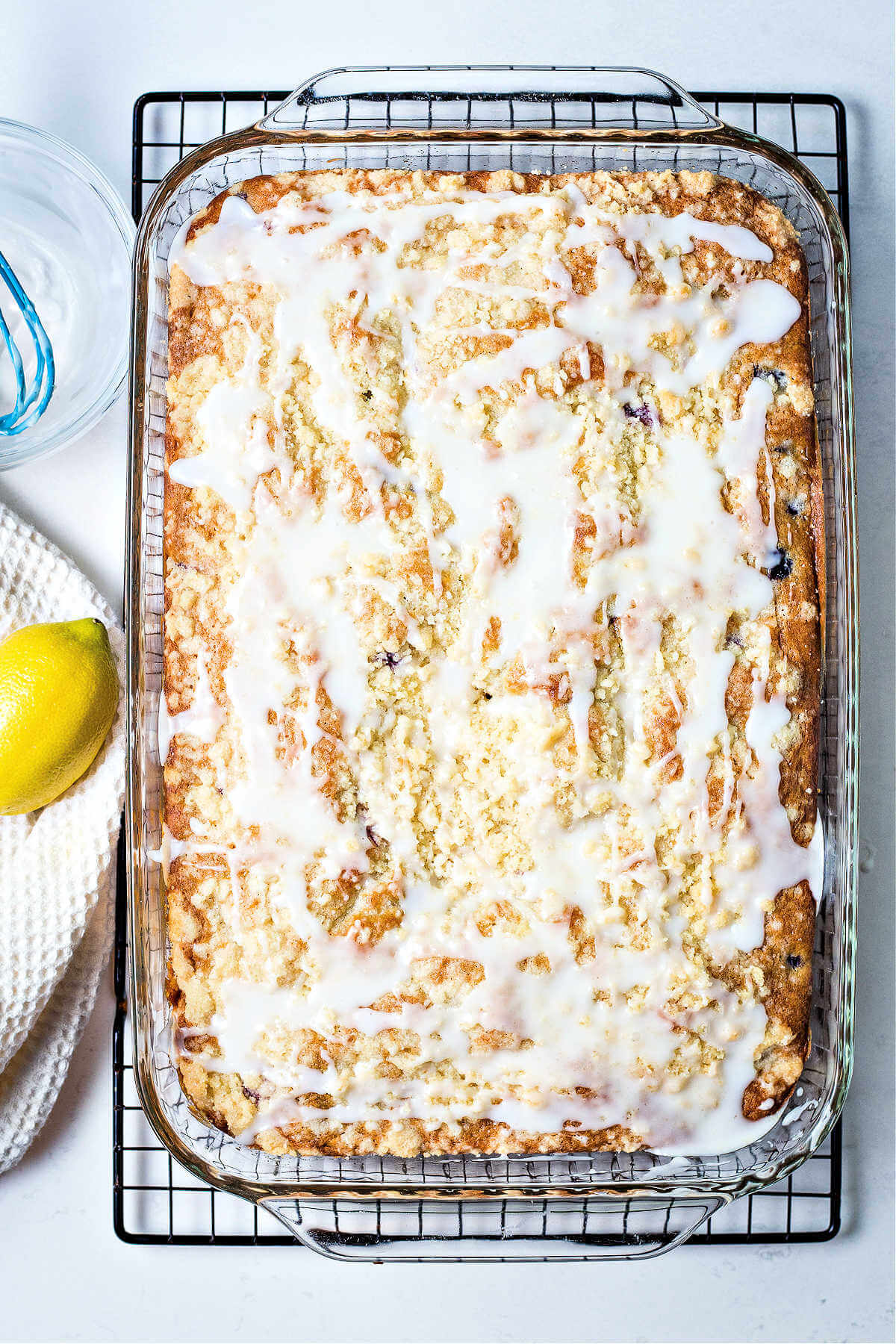 a glazed blueberry crumb cake in a 9x13 inch glass baking dish on a cooling rack.