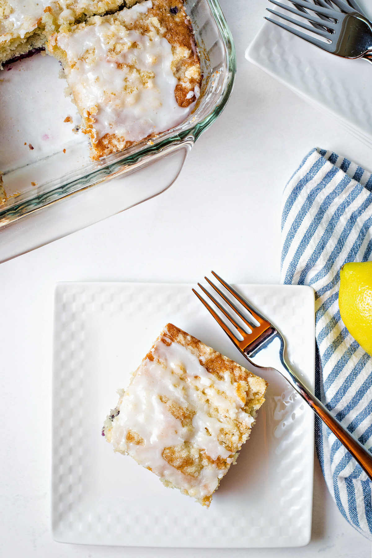 a slice of blueberry crumb cake on a plate with a fork and the rest of the cake in the background.