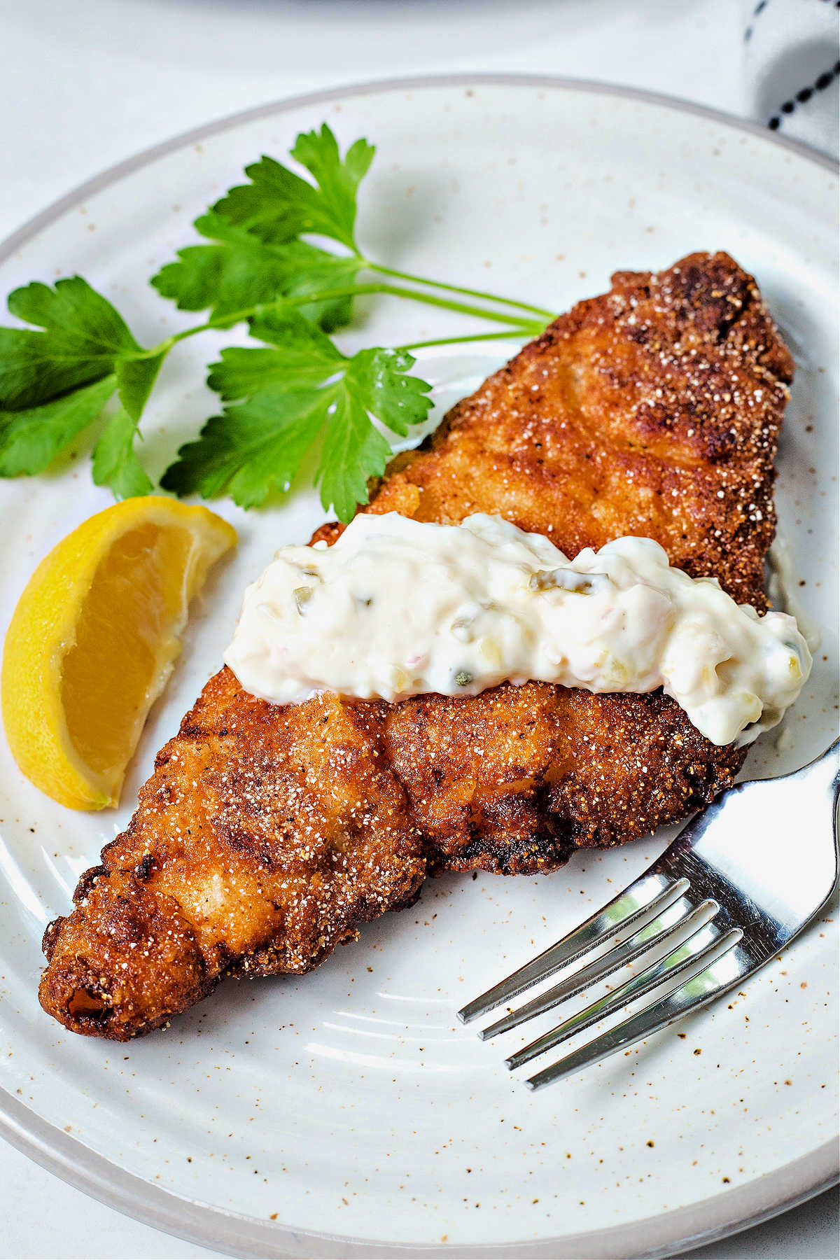 fried catfish on a plate drizzled with tartar sauce.