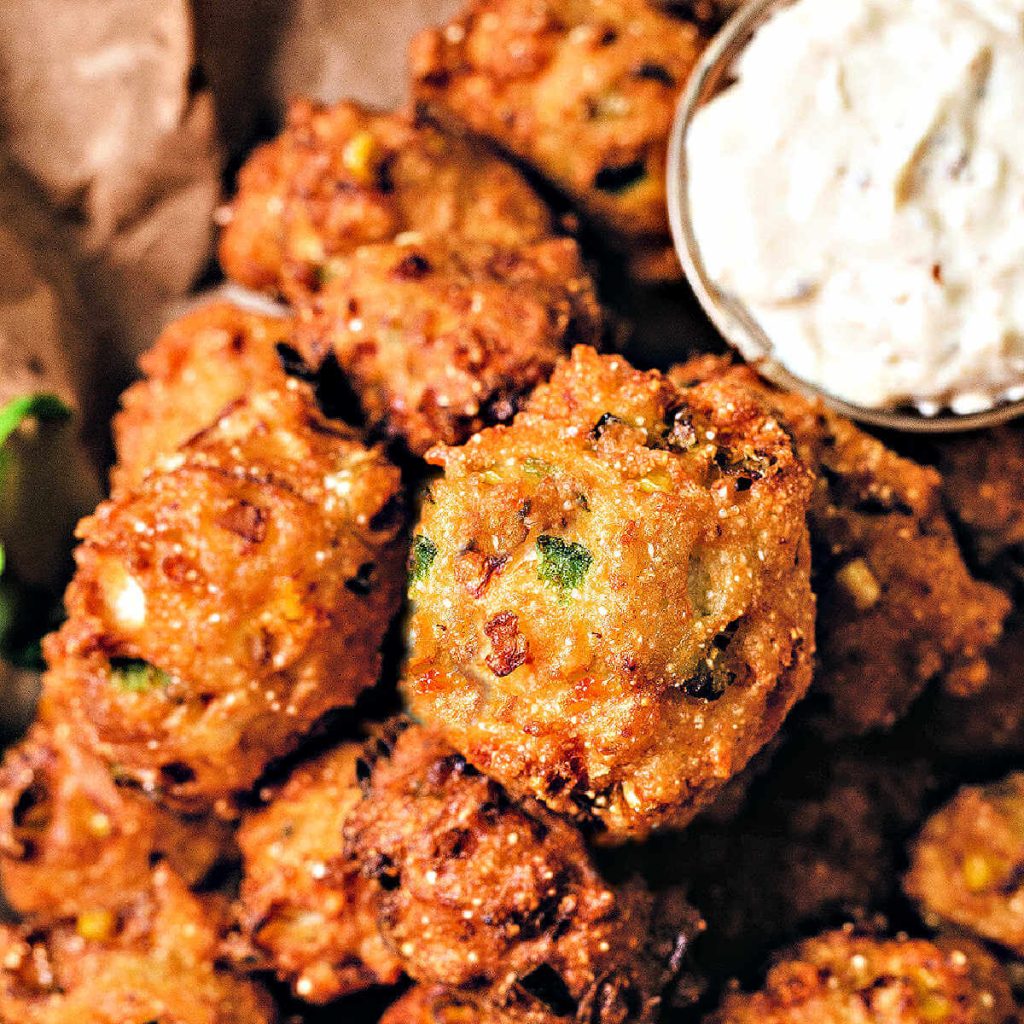 fried hush puppies in a paper lined basket with old bay sauce.