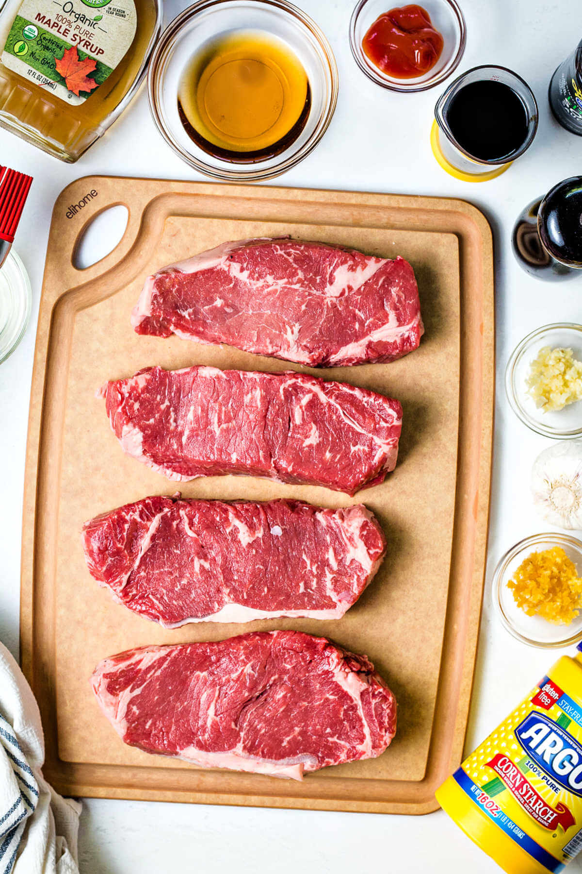 4 sirloin strip steaks on a cutting board with ingredients for Mongolian glazed steak surrounding.