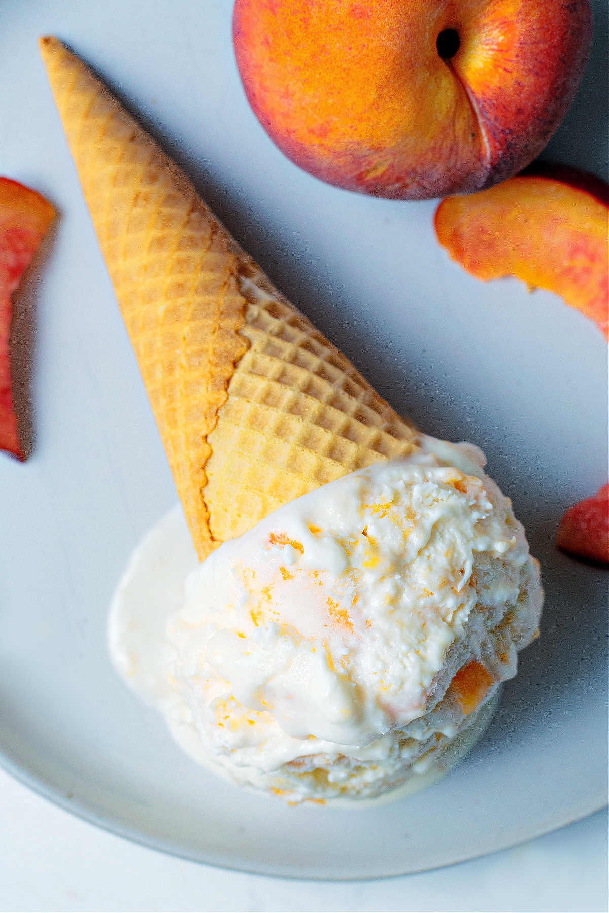 a scoop of peach ice cream on a sugar cone laying on a plate.