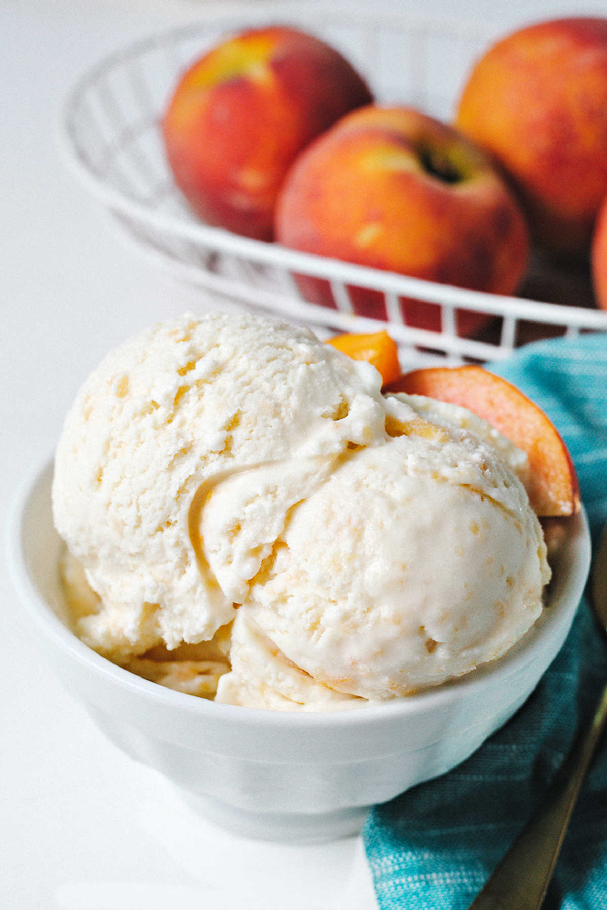 a bowl of peach ice cream with a basket of peaches in the background.