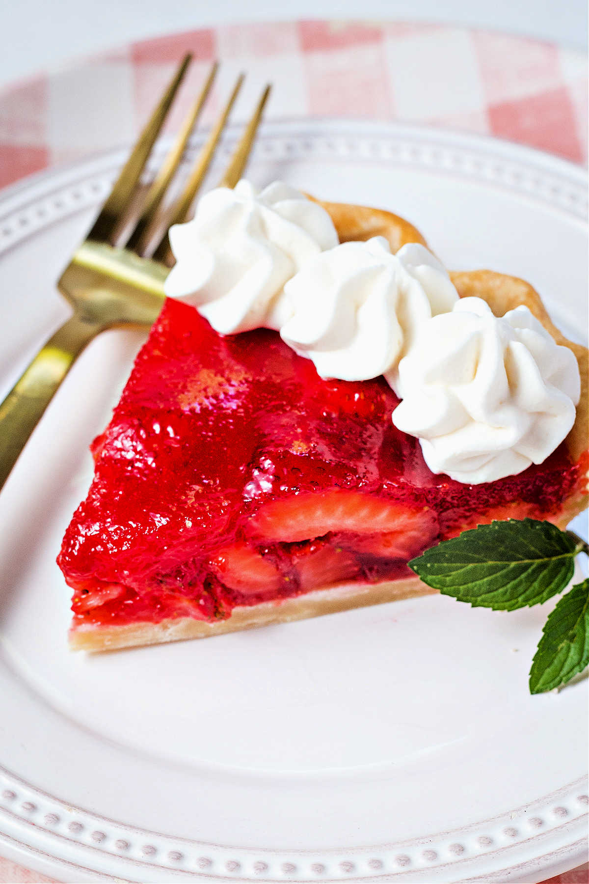 a slice of strawberry pie with dollops of whipped cream and a sprig of mint on a plate.
