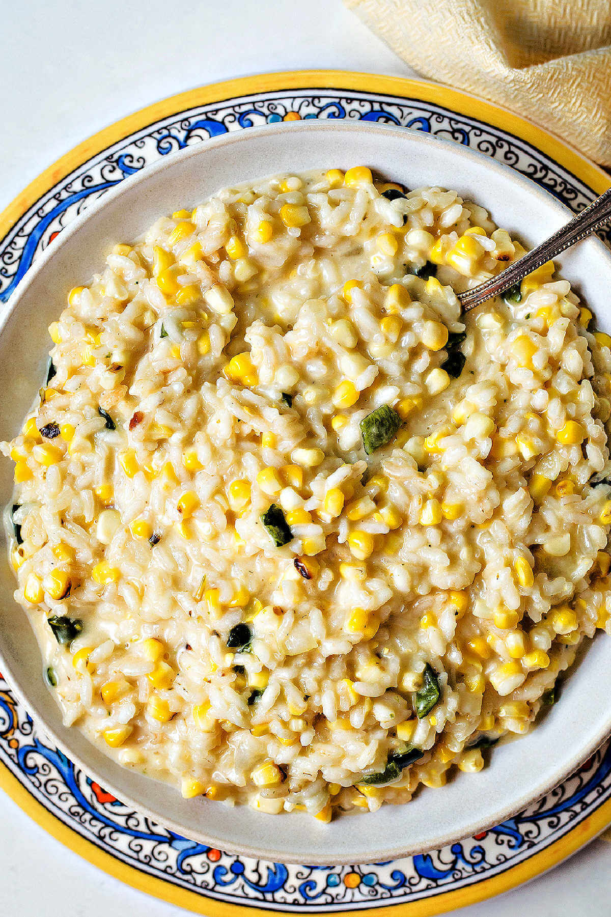 arroz poblano in a bowl sitting on a decorative plate on a table with a spoon.