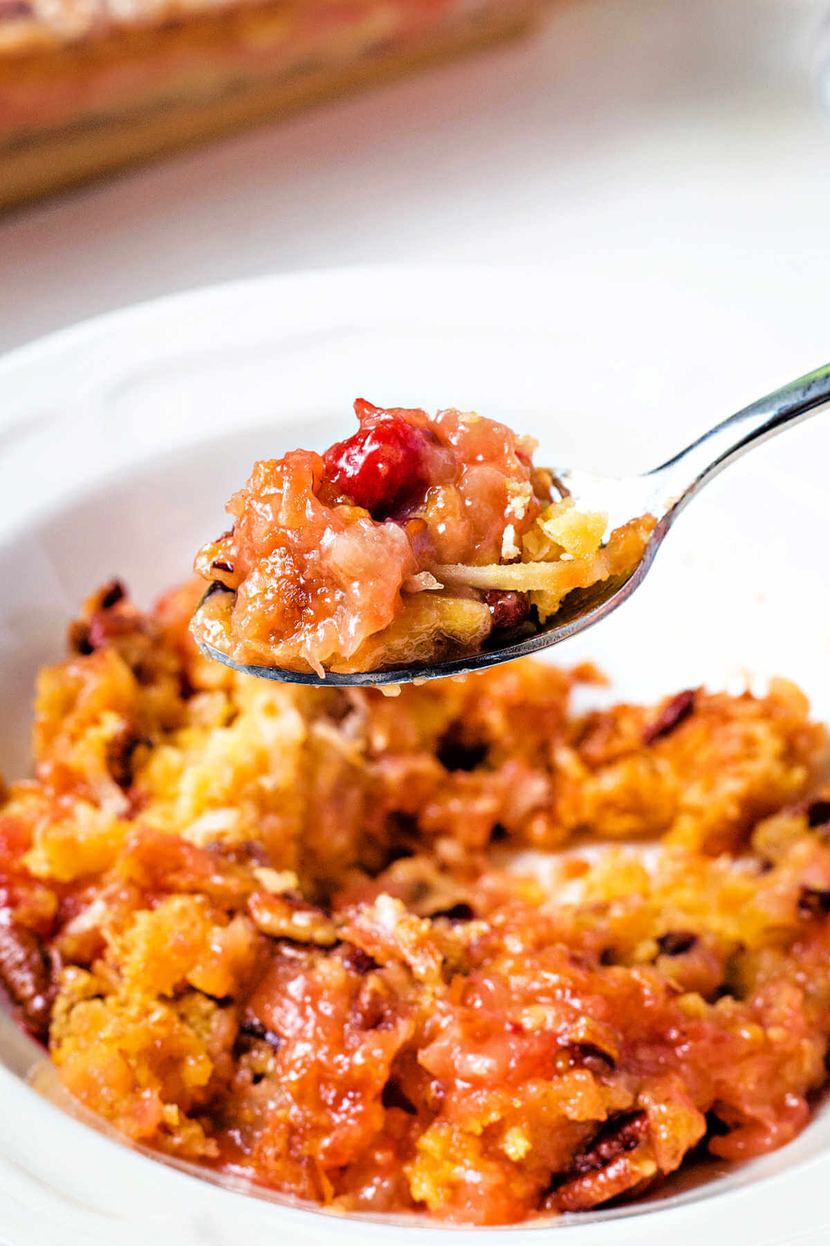 a spoon lifting a bite of cherry dump cake out of a bowl.