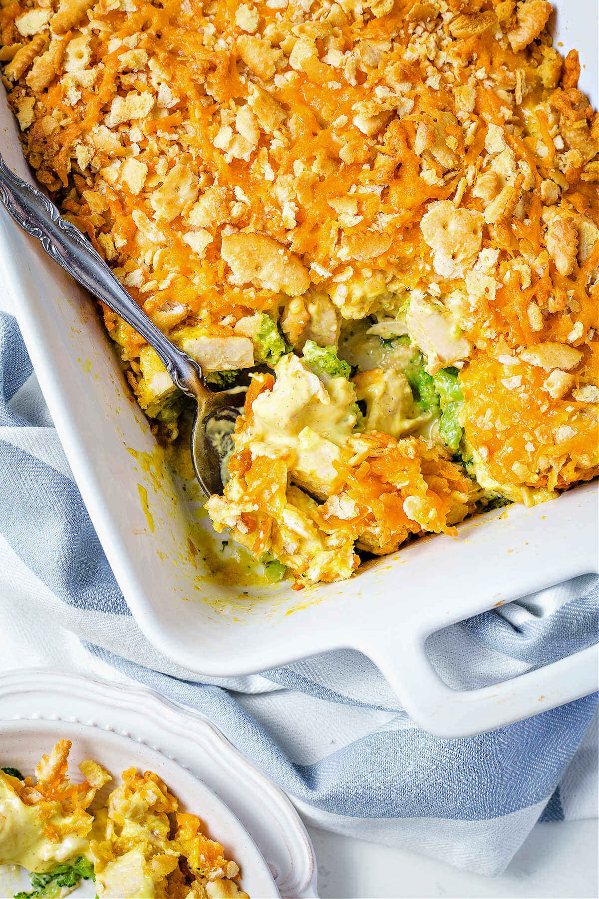 a serving spoon inserted into a baked chicken broccoli casserole and a serving plate to the side.