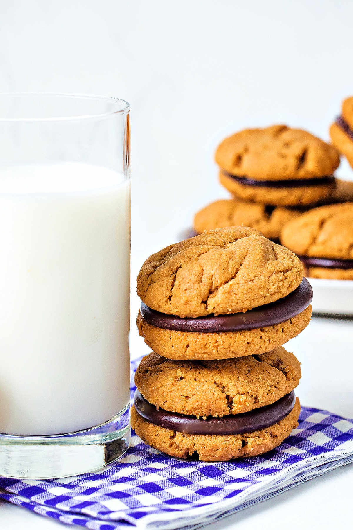 peanut butter sandwich cookies stacked on a gingham napkin with a glass of milk.