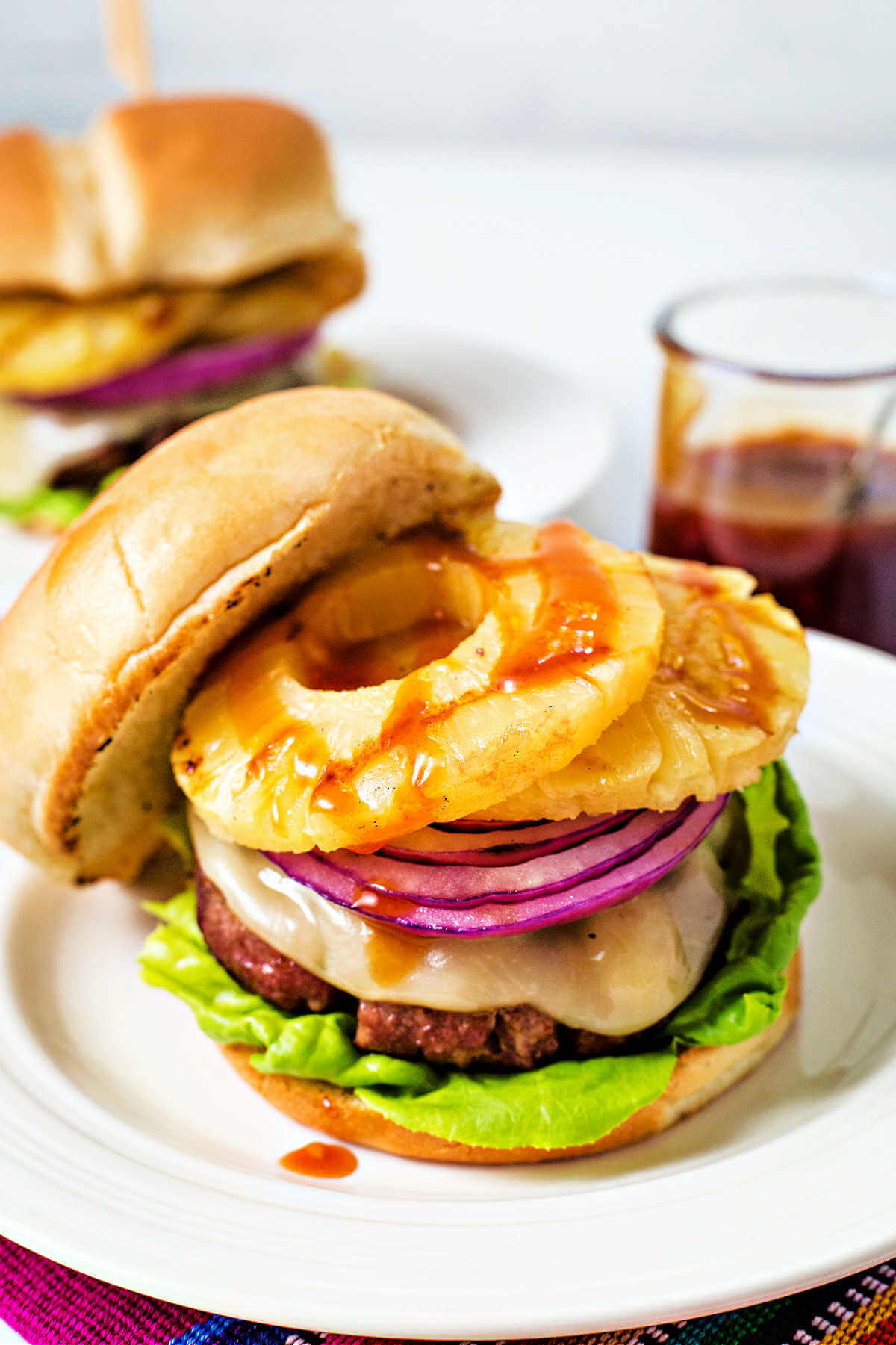 an open face hawaiian burger with provolone cheese, grilled pineapple, and red onion and drizzled with sauce on a plate.