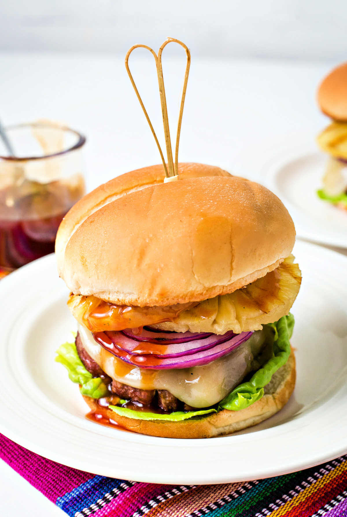 a hawaaian burger on a white plate sitting on a colorful place mat.