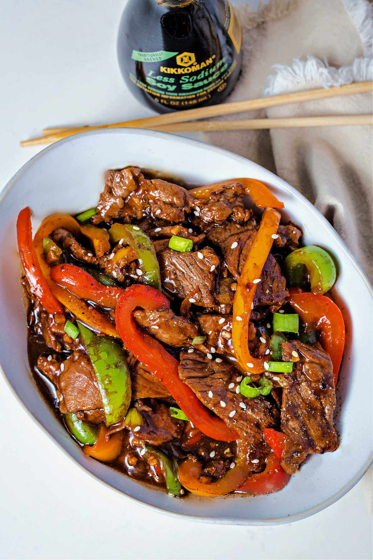 pepper steak in a white serving bowl with chopsticks and soy sauce on the table.