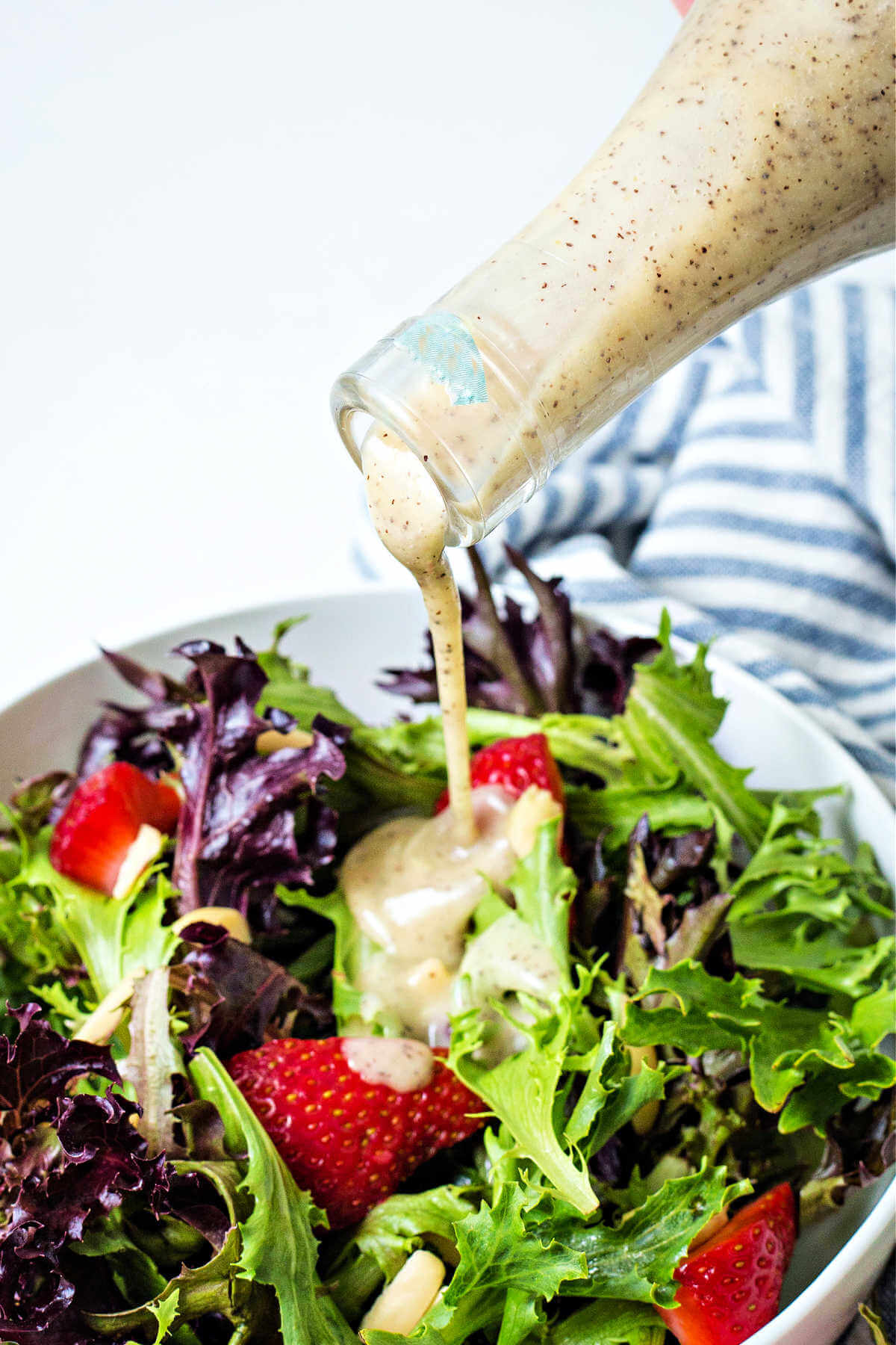 pouring poppy seed dressing over a salad of spring mix and strawberries.