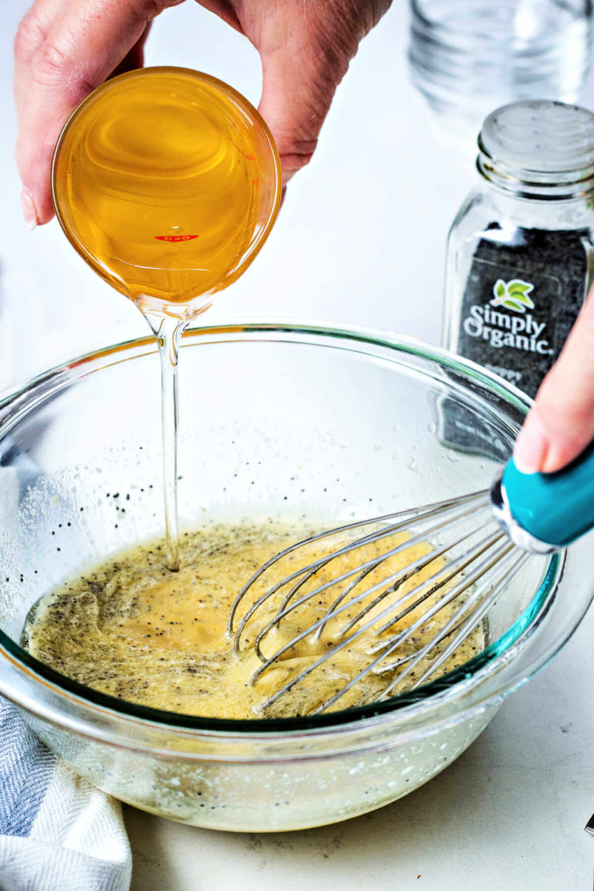 olive oil being poured in a slow stream while whisking into a bowl of poppy seed dressing.