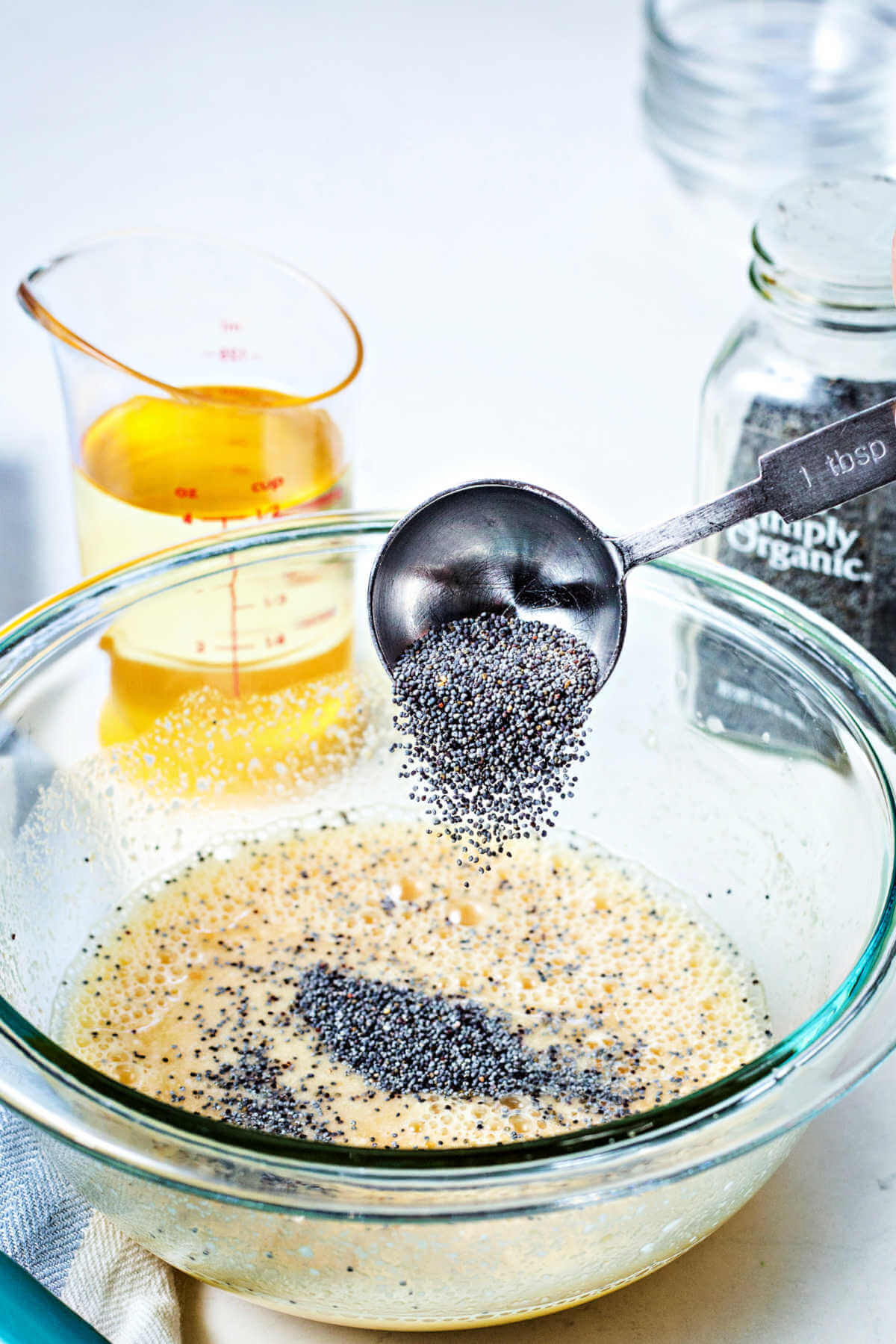 a tablespoon of poppy seeds being added into a bowl of dressing.