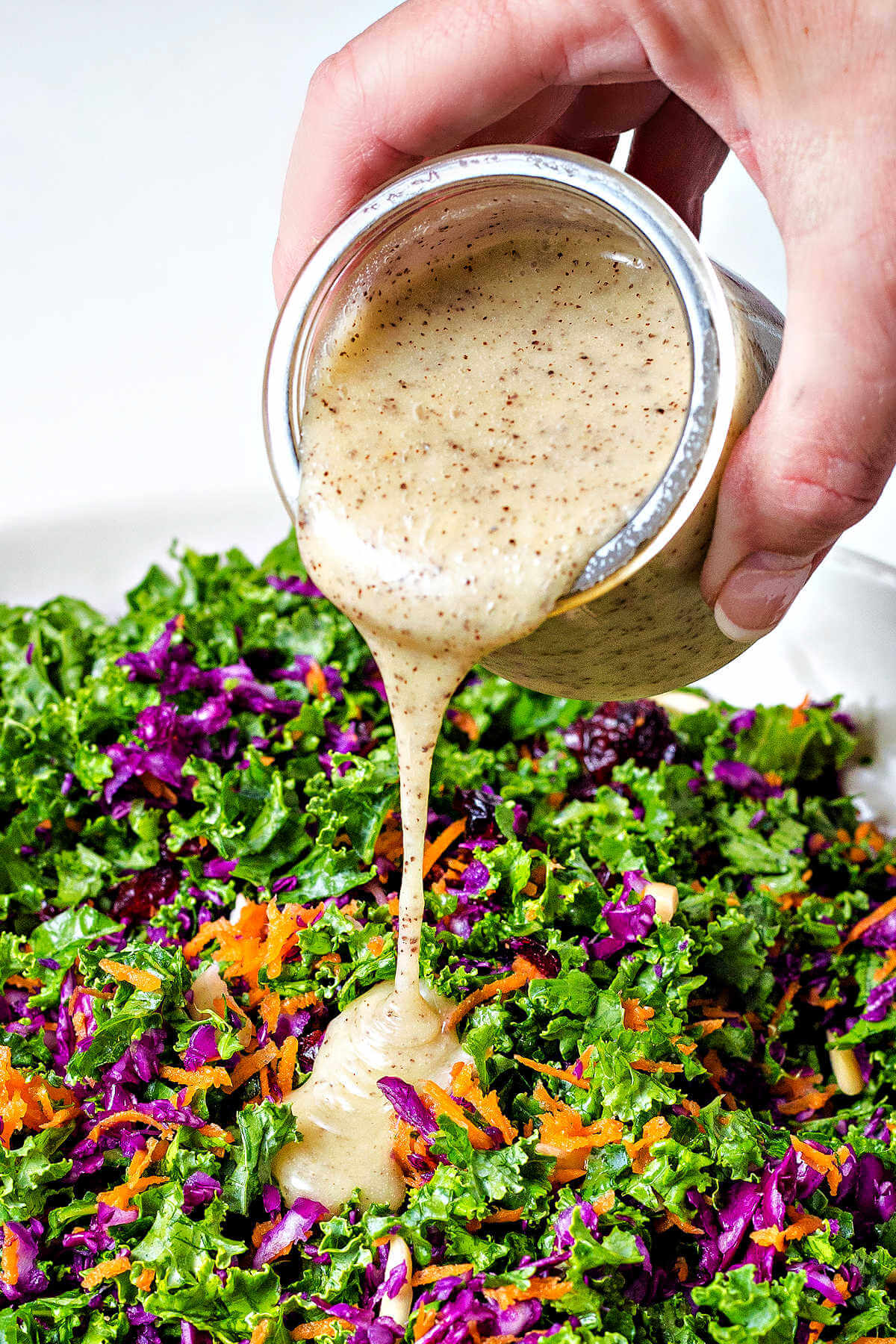 pouring poppy seed dressing over a bowl of kale salad.