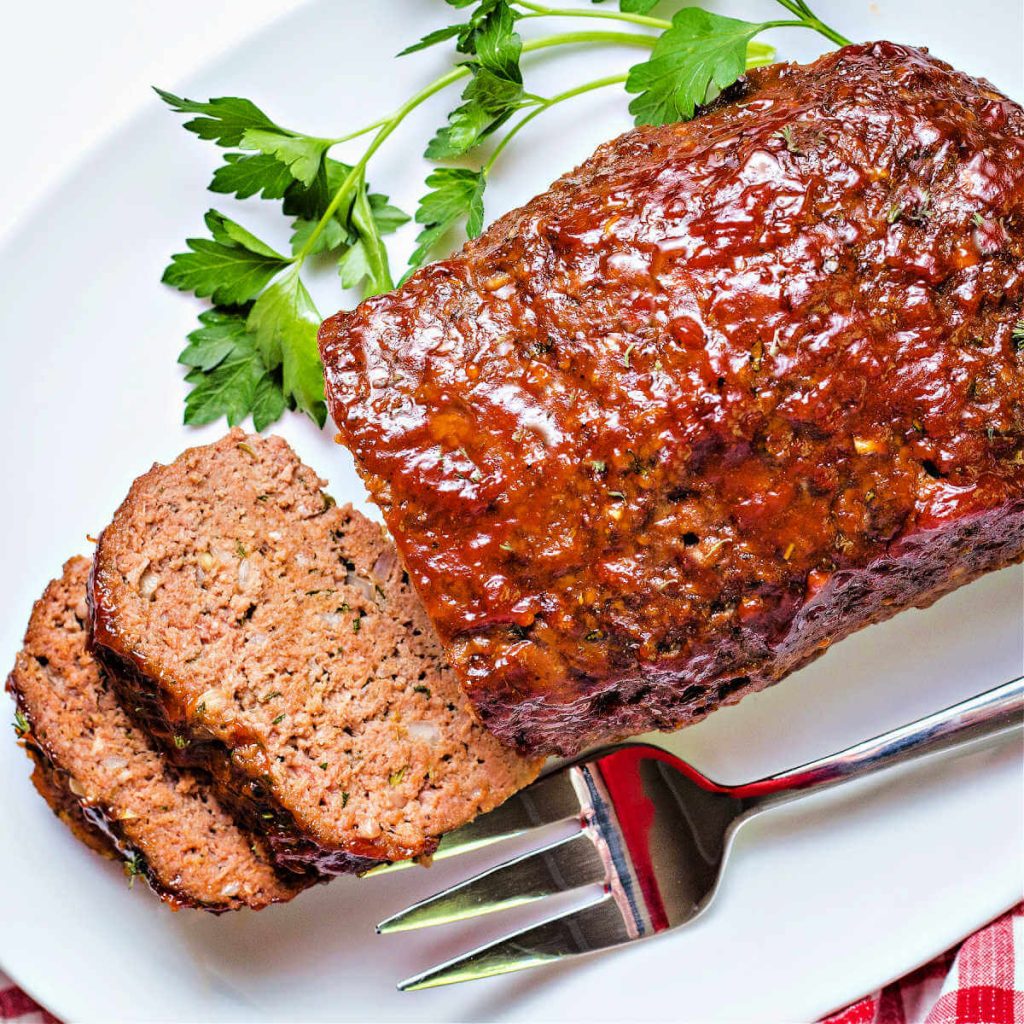 slices of smoked meatloaf on a serving platter with a meat fork.