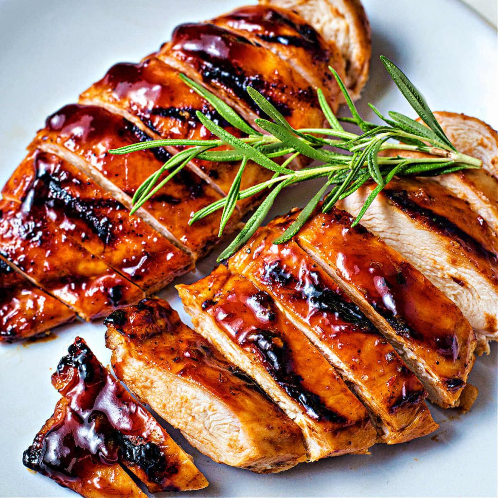 sliced grilled balsamic chicken on a plate garnished with fresh rosemary.