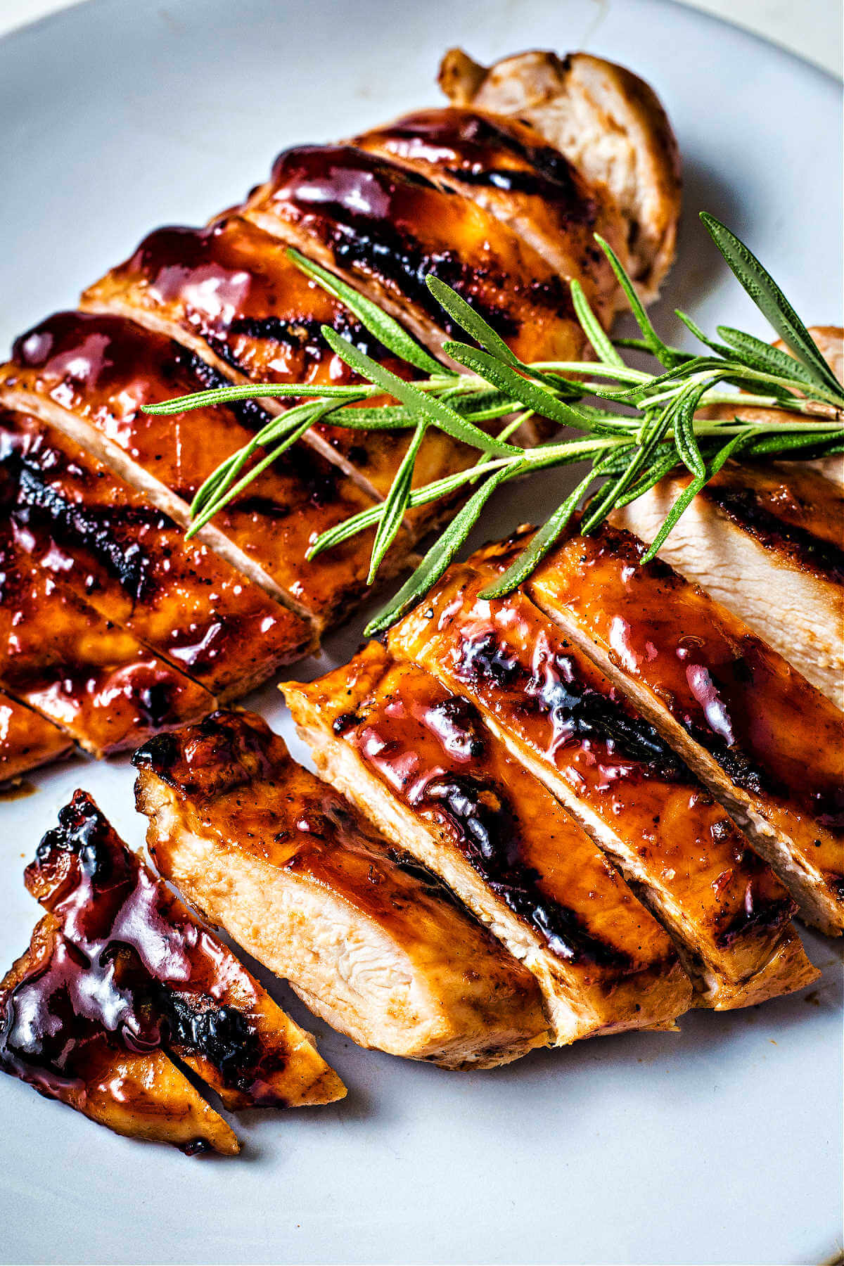 sliced grilled balsamic chicken on a plate garnished with fresh rosemary.