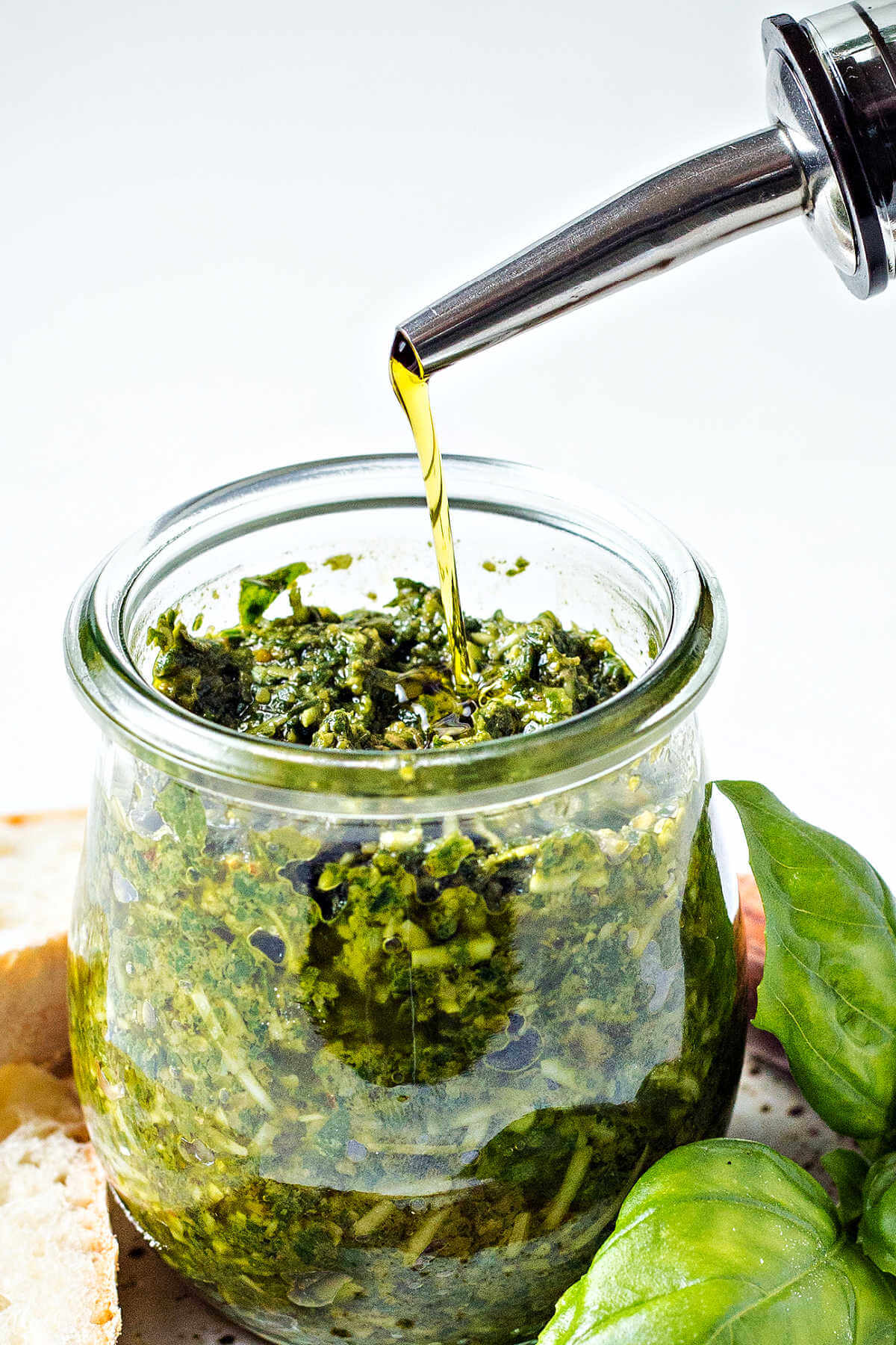 pouring olive oil over the top of a jar of pesto.