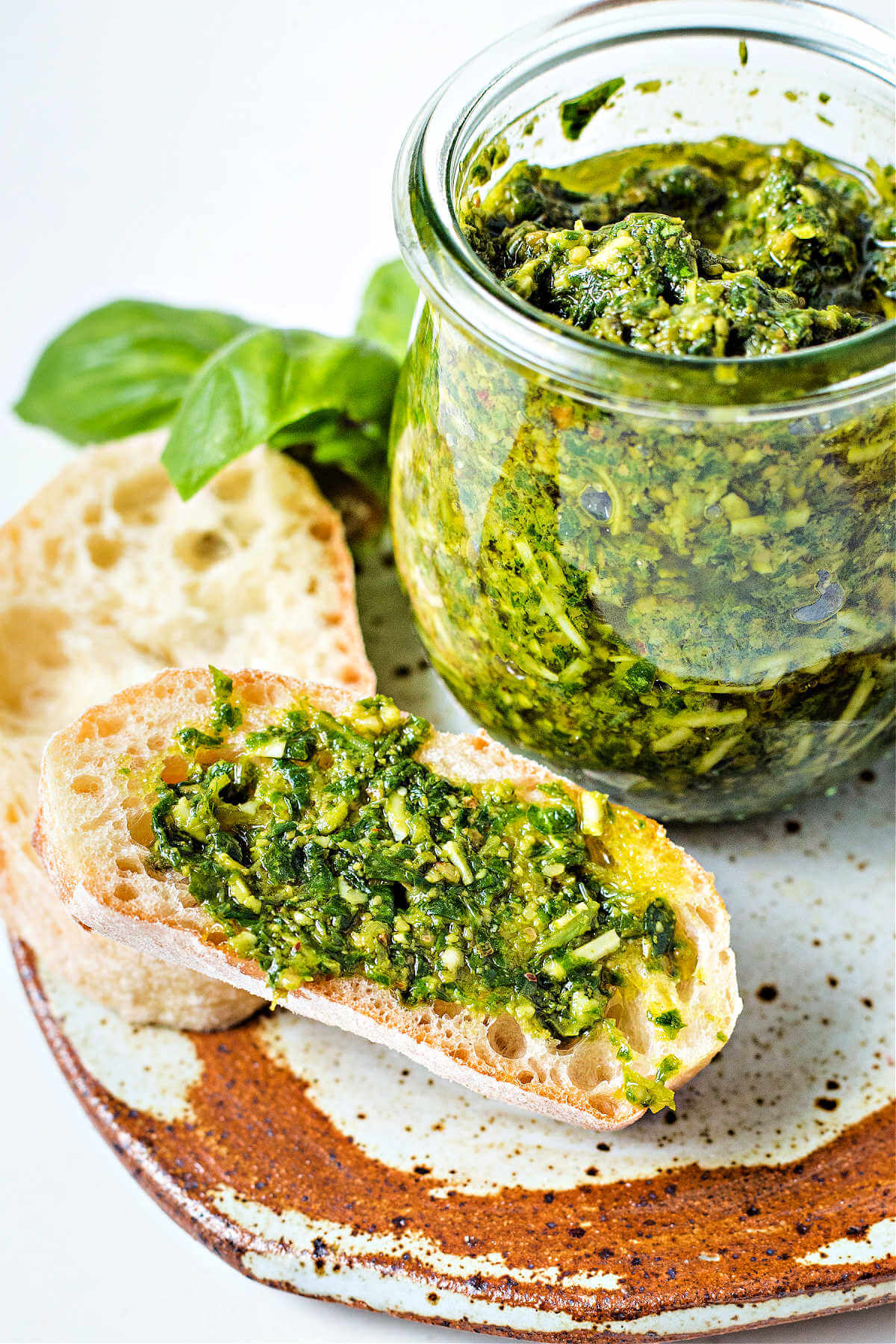 a slice of baguette with pesto spread on top sitting on a plate with a jar of pesto.