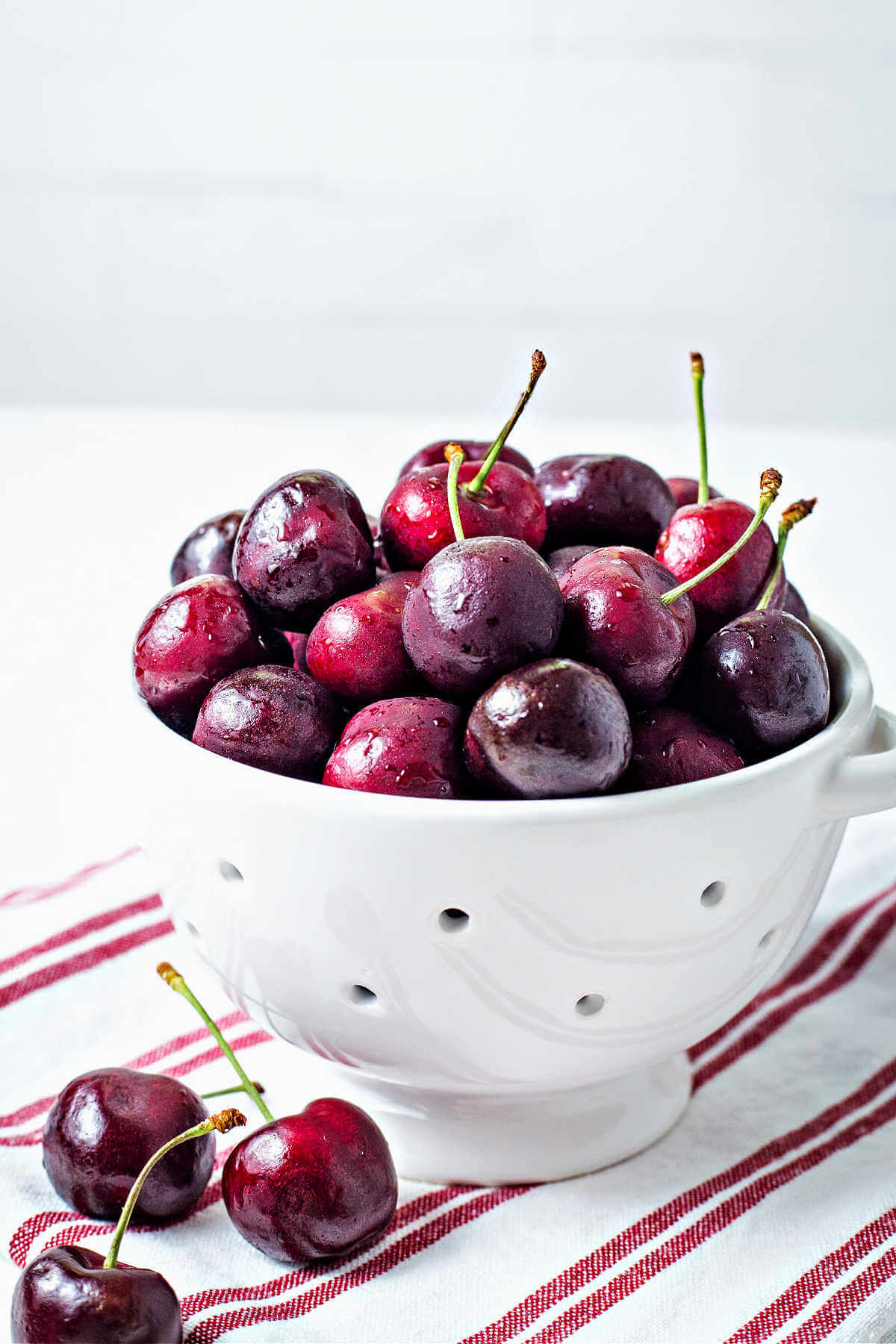 bing cherries in a white colander on a tea towel on a counter.