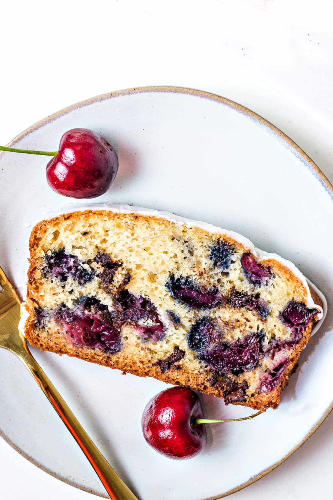a slice of cherry bread on a serving plate with a fork and cherries.