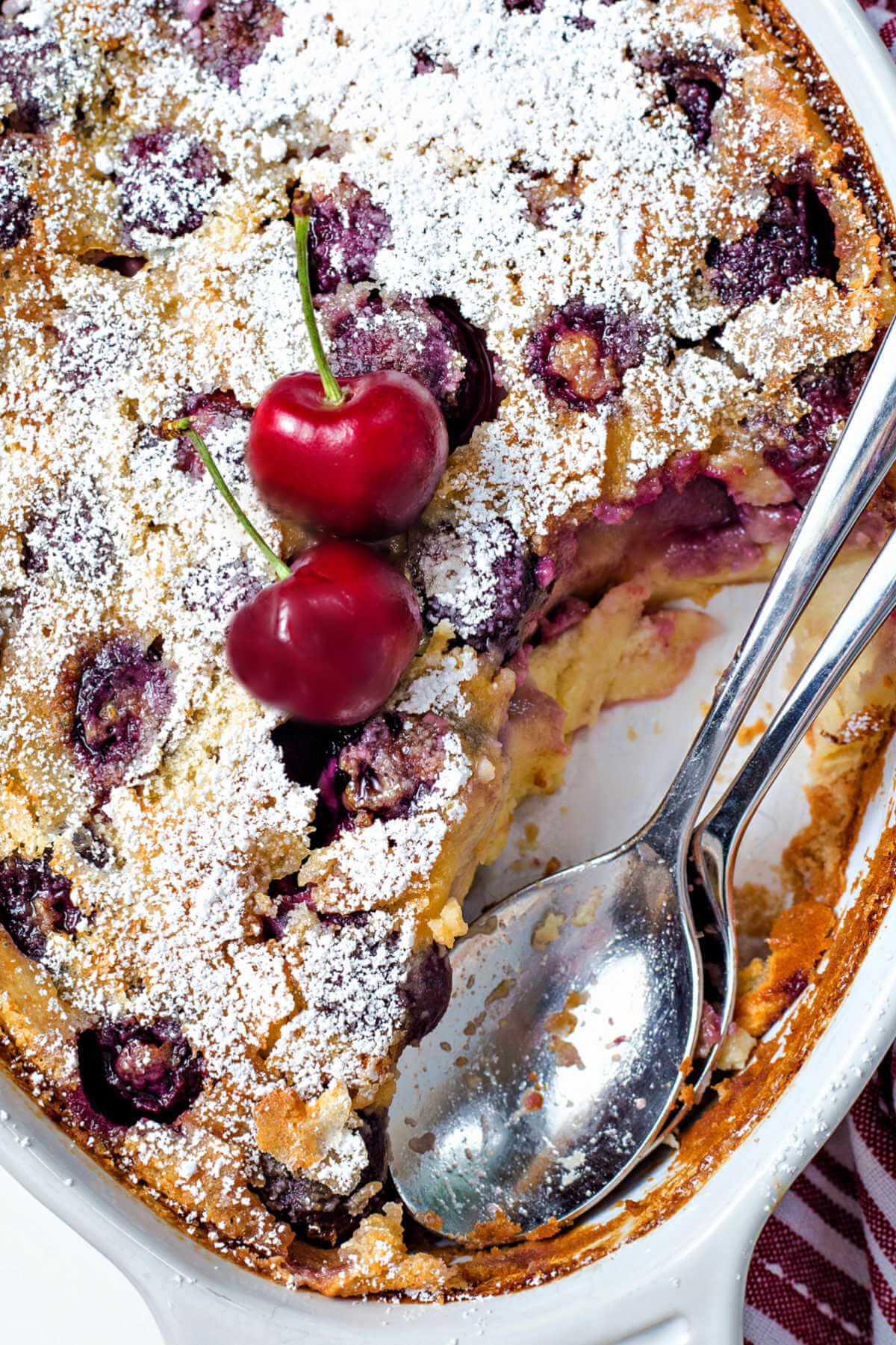 cherry clafoutis with two serving spoons and a serving missing from the pan.
