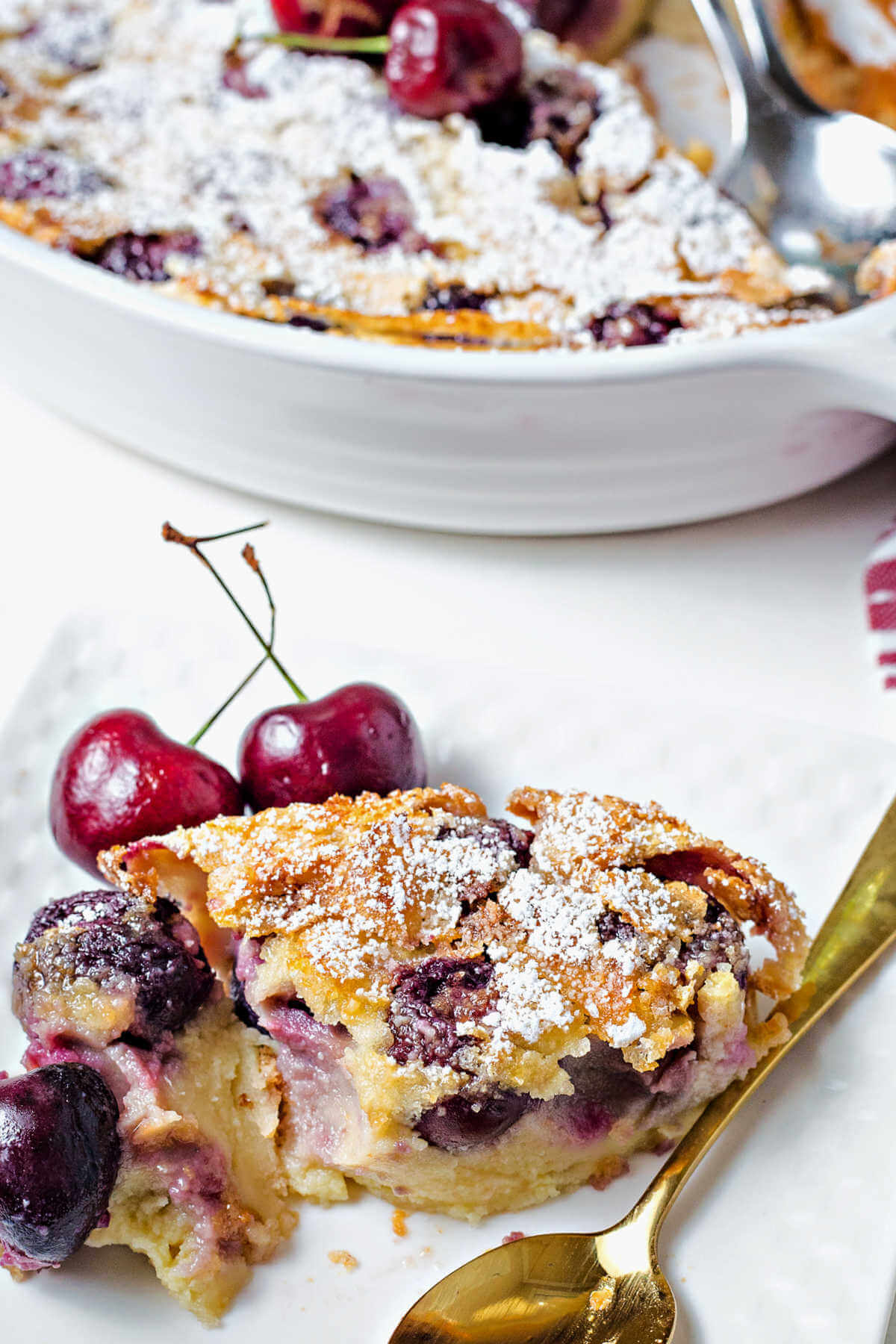 a half eaten serving of cherry clafoutis on a plate with a gold spoon.