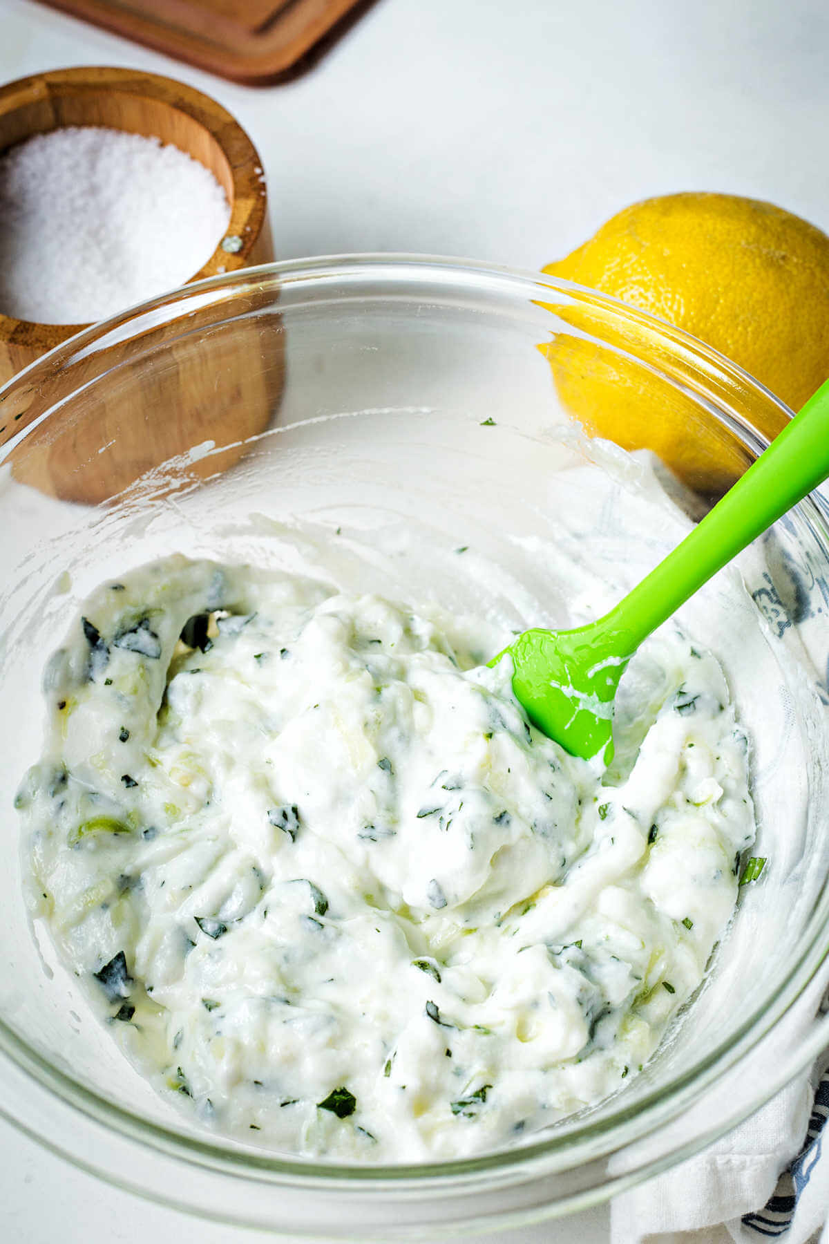 stirring together the ingredients for Tzatziki sauce in a glass bowl.