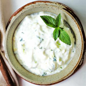 a bowl of cucumber sauce garnished with fresh mint spring.