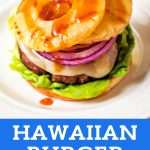 an open face hawaiian burger with provolone cheese, grilled pineapple, and red onion and drizzled with sauce on a plate.