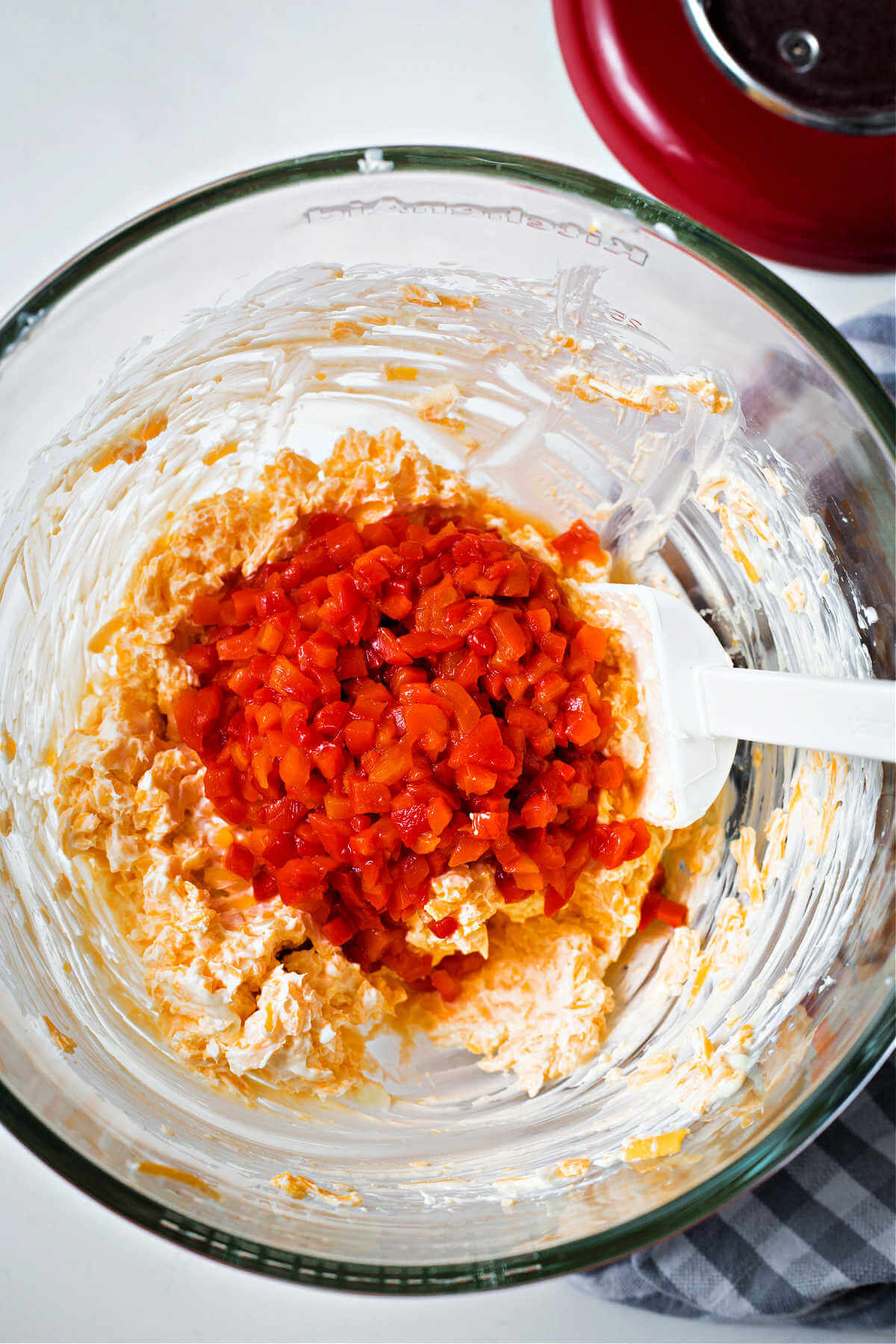 adding diced pimentos to a bowl of creamed cheese and cheddar cheese.