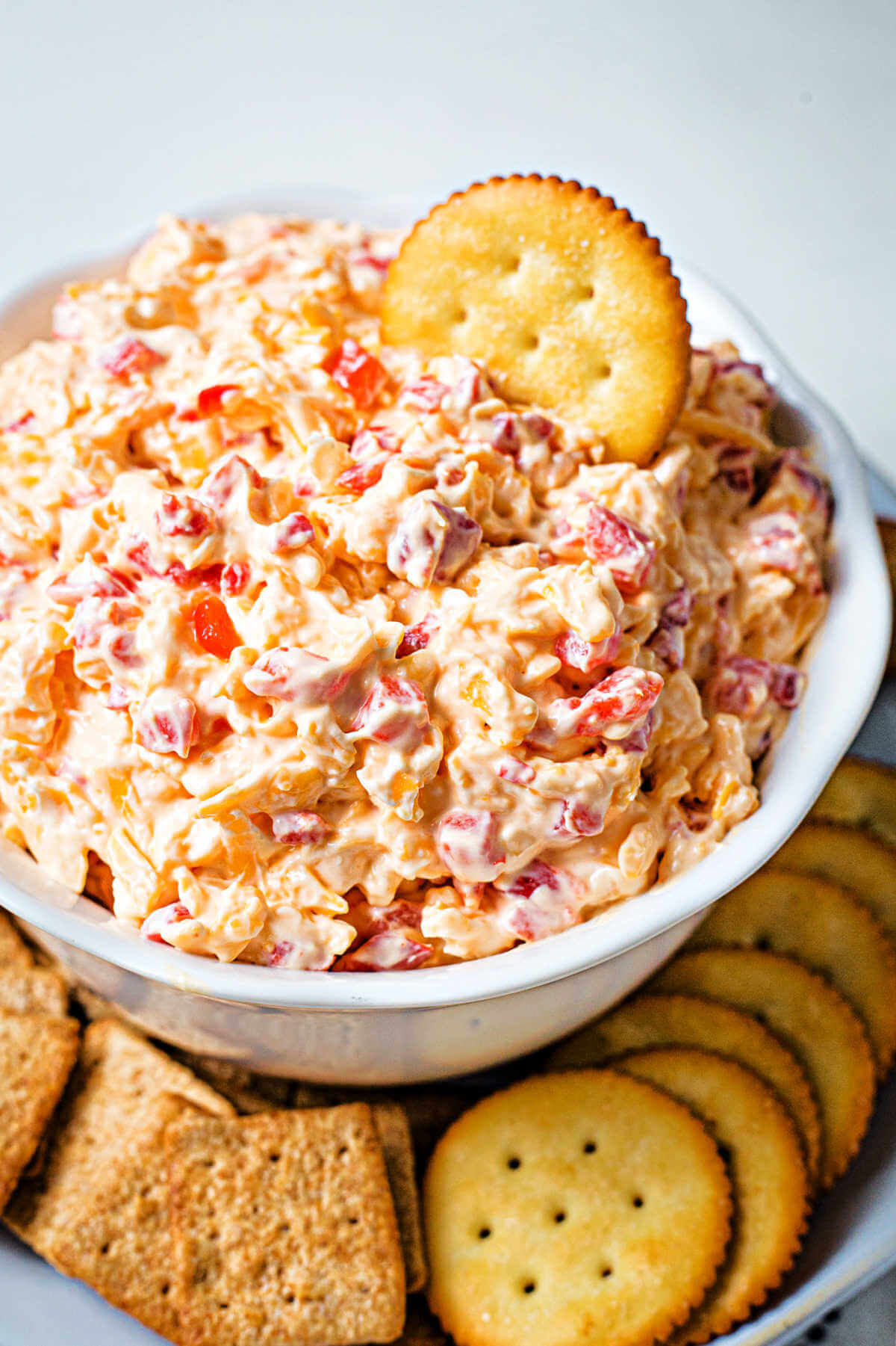 a bowl mounded full with homemade pimento cheese with crackers on a plate.