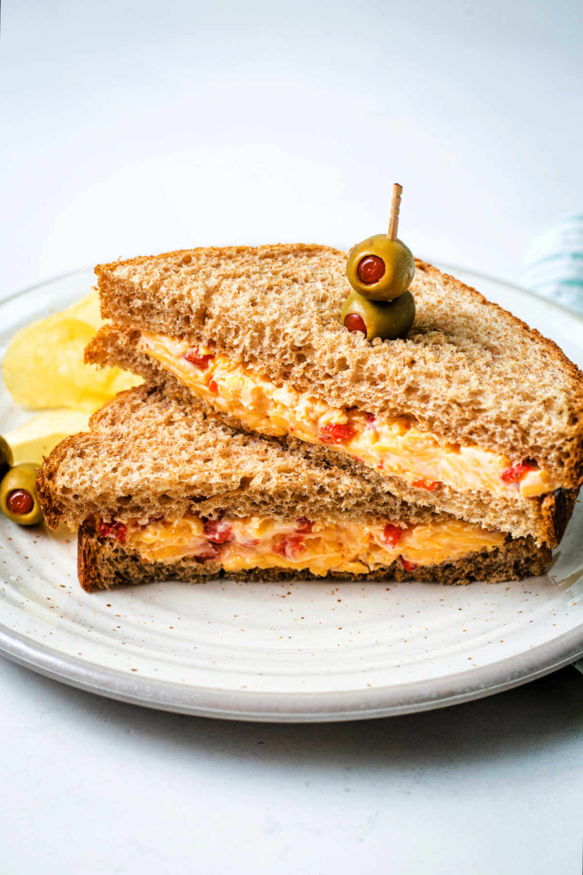 a pimento cheese sandwich cut in half on a plate with olives and potato chips.