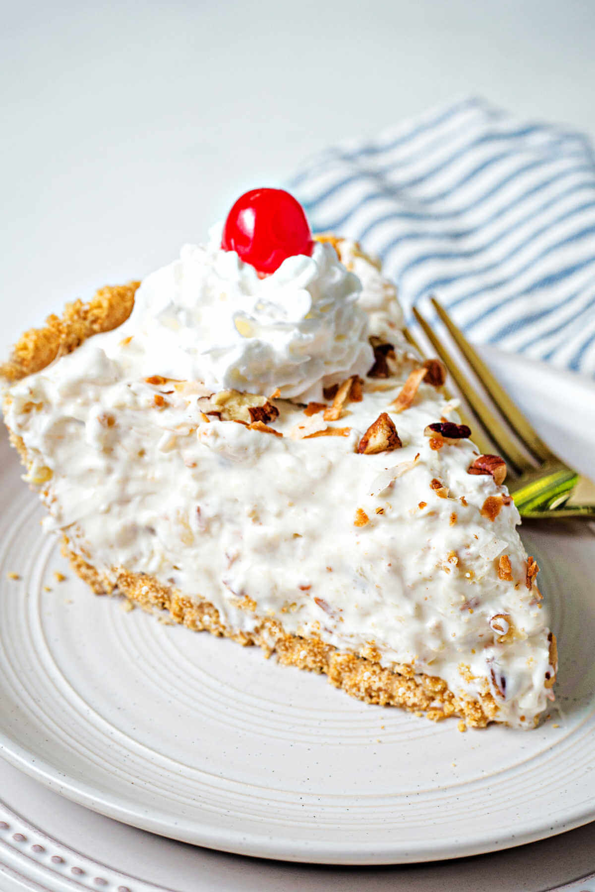 a slice of million dollar pie garnished with whipped cream and a cherry on a plate with a fork.
