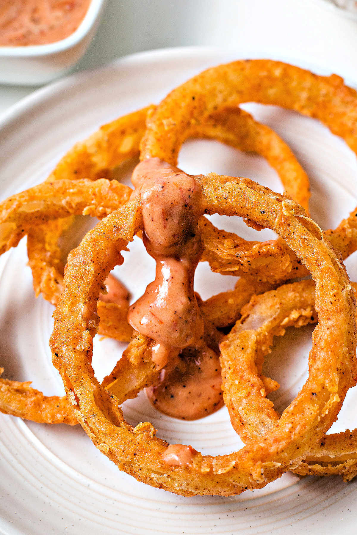 a mound of onion rings on a plate drizzled with onion ring sauce.