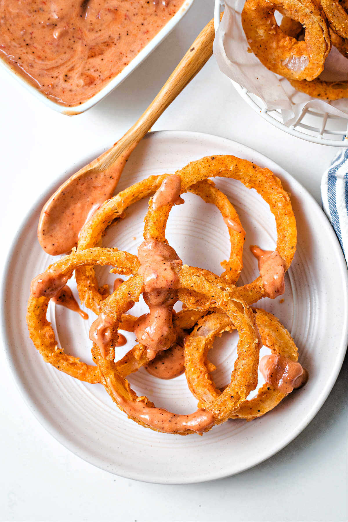 a mound of onion rings on a plate drizzled with onion ring sauce with a spoon to the side.