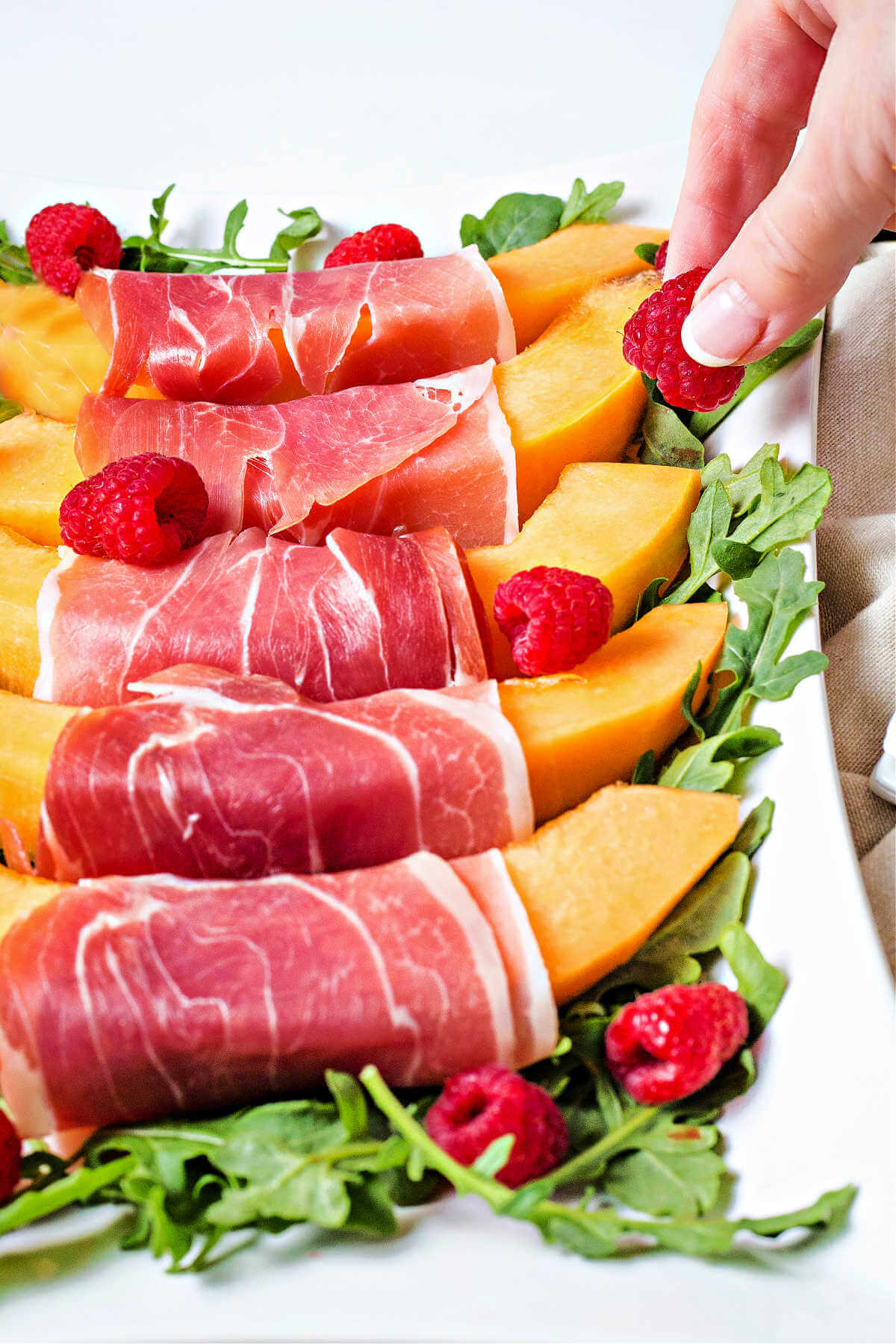 placing a raspberry on a platter of melon with prosciutto.