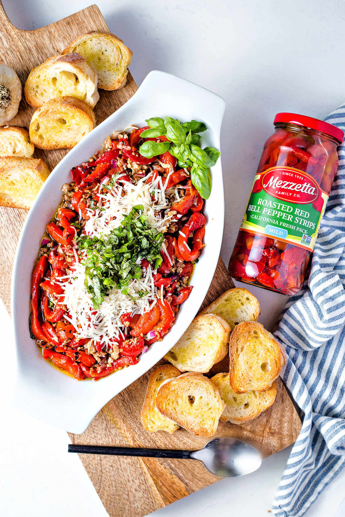 a serving dish filled with red pepper and bacon bruschetta with basil garnish and a jar of Mezzetta roasted red pepper strips in the background.