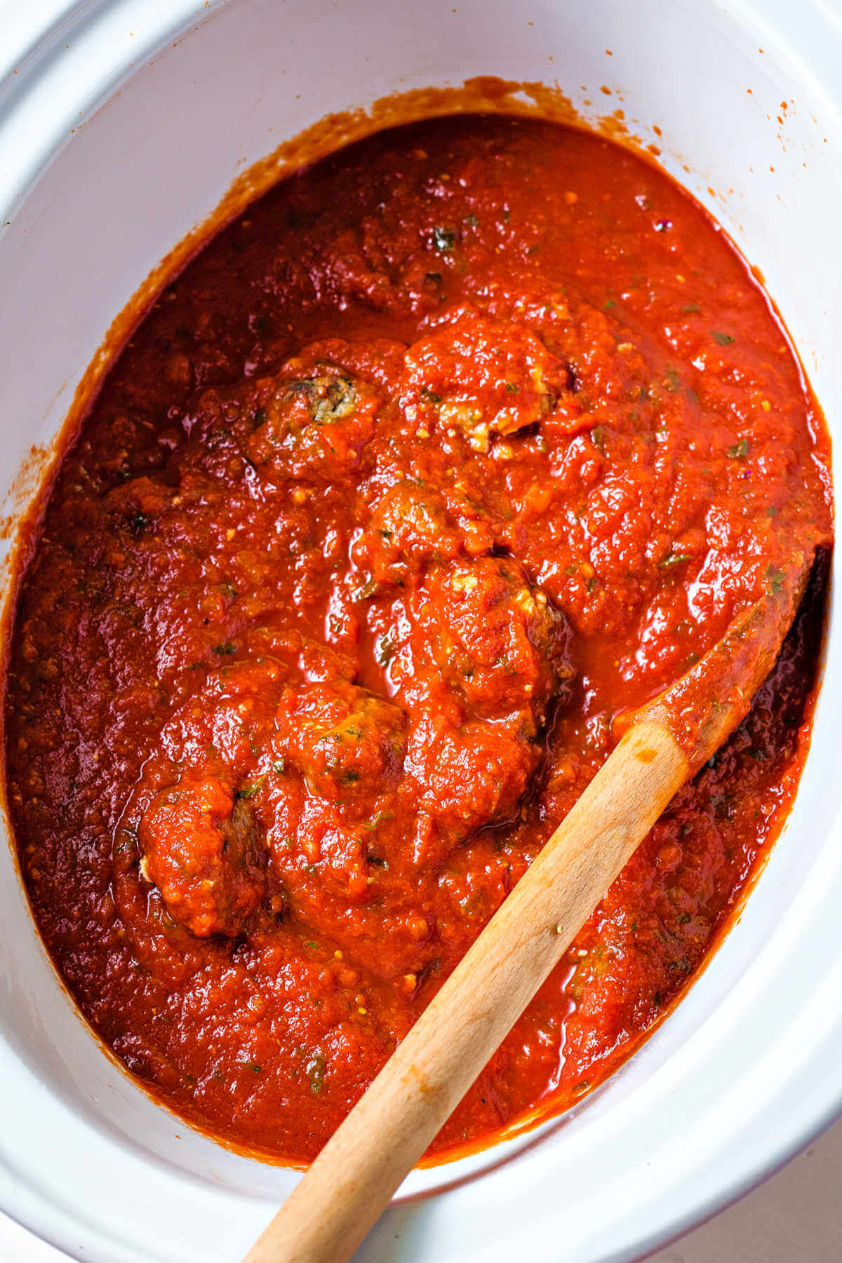 meatballs in marinara in a slow cooker with a wooden spoon.