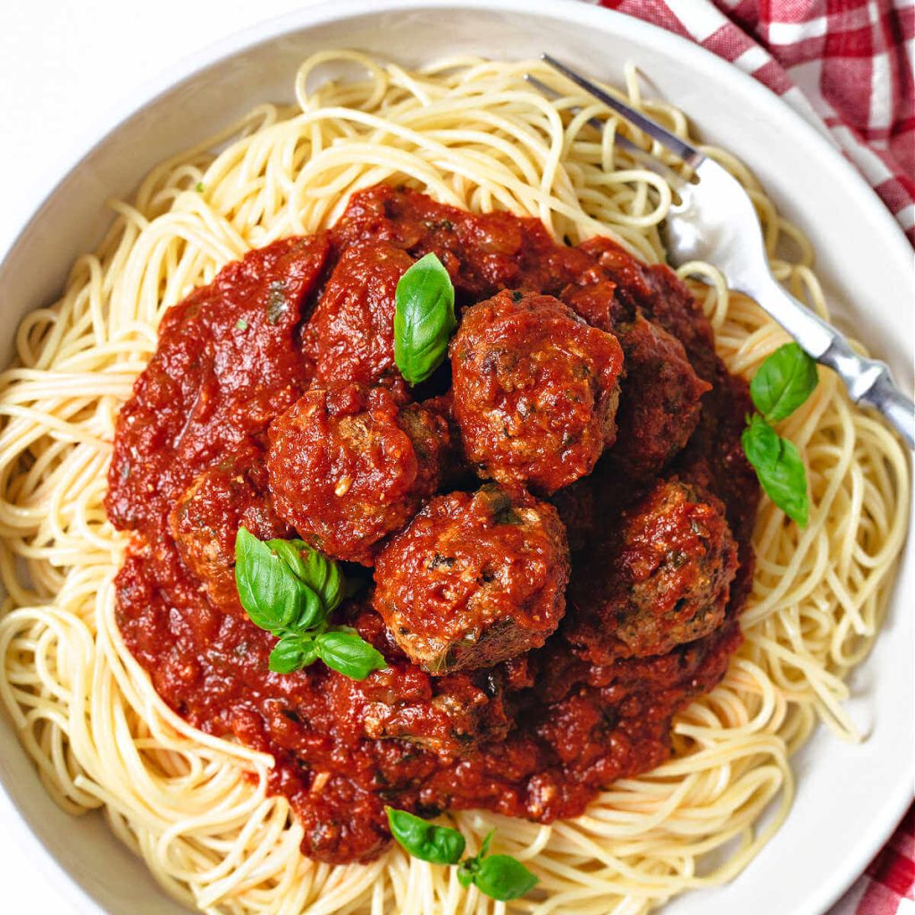 a plate of spaghetti topped with marinara sauce and meatballs with sprigs of basil.