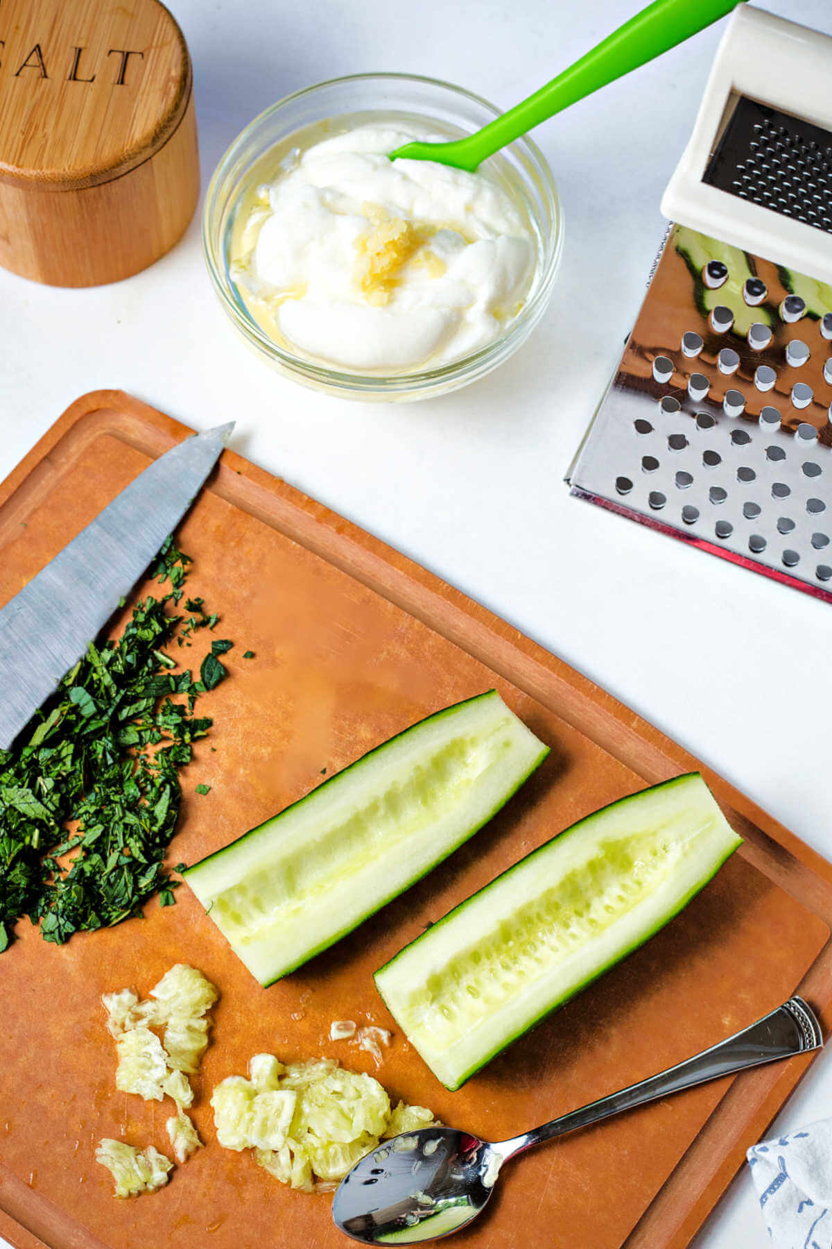 a halved cucumber with the seeds scooped out and a spoon on a cutting board.
