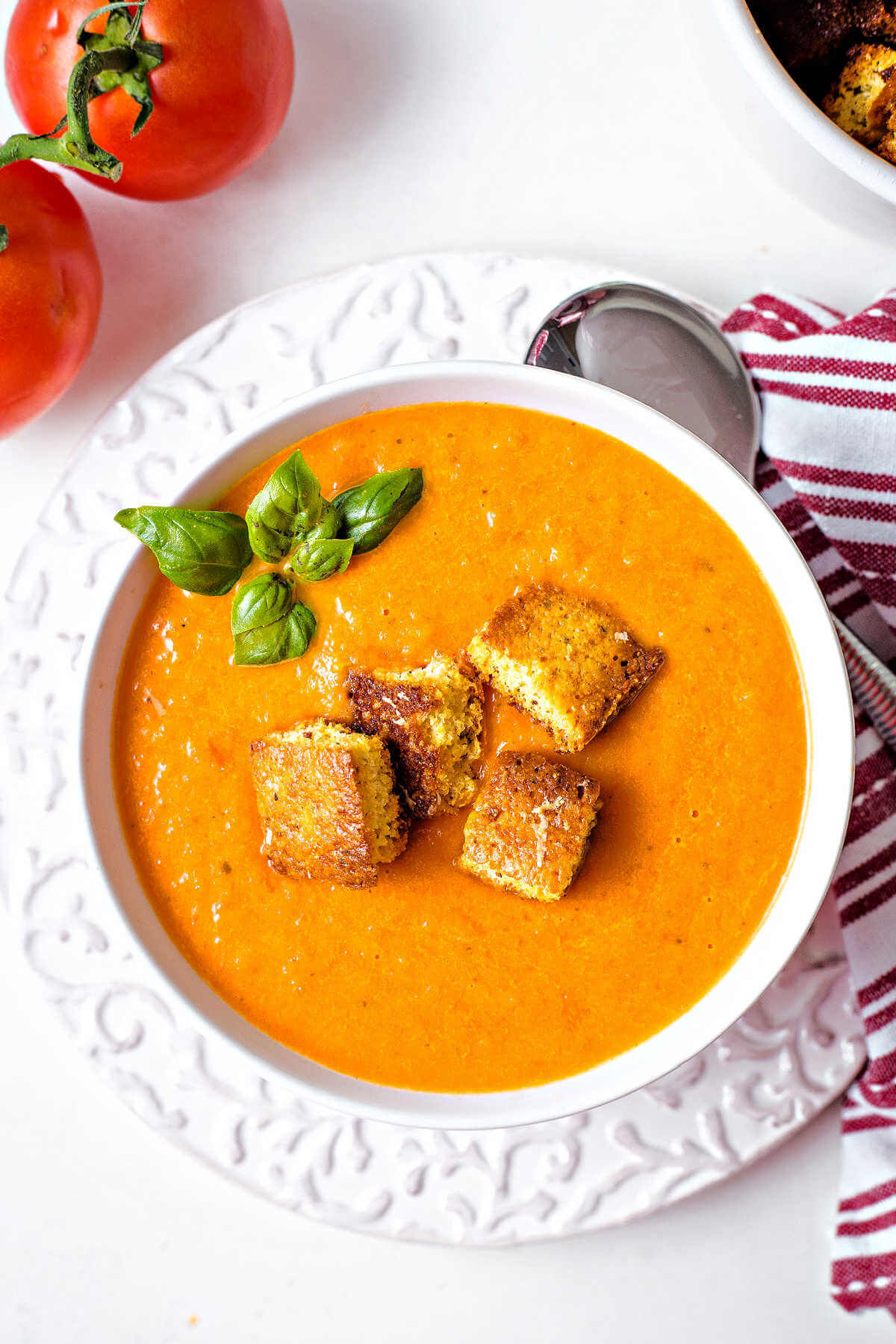 a bowl of creamy tomato soup garnished with a sprig of basil and topped with cornbread croutons.