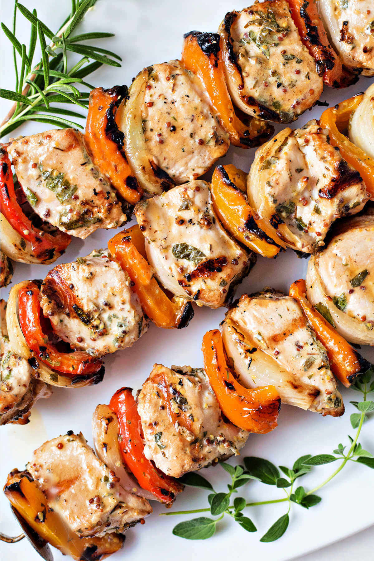 close up image of greek chicken kabobs on a white platter.