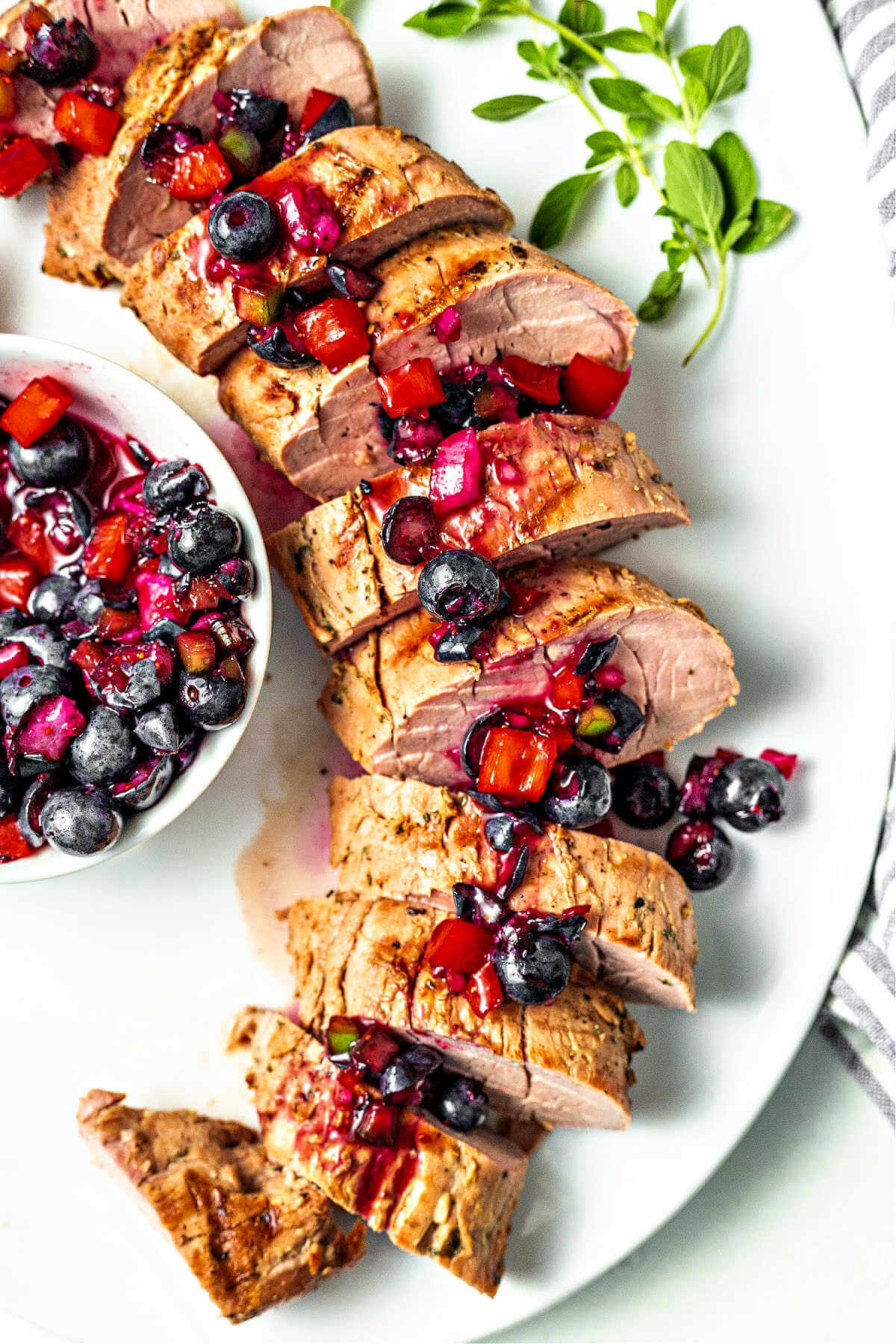 blueberry salsa drizzled over slices of grilled pork tenderloin on a platter.